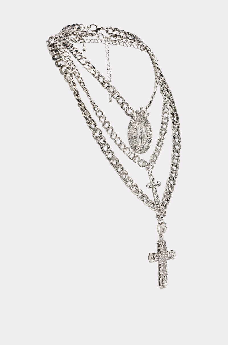 The PRAY FOR YOU NECKLACE SET features a layered silver chain with a jeweled cross pendant and an oval Virgin Mary medallion, displayed on a plain white background. 2