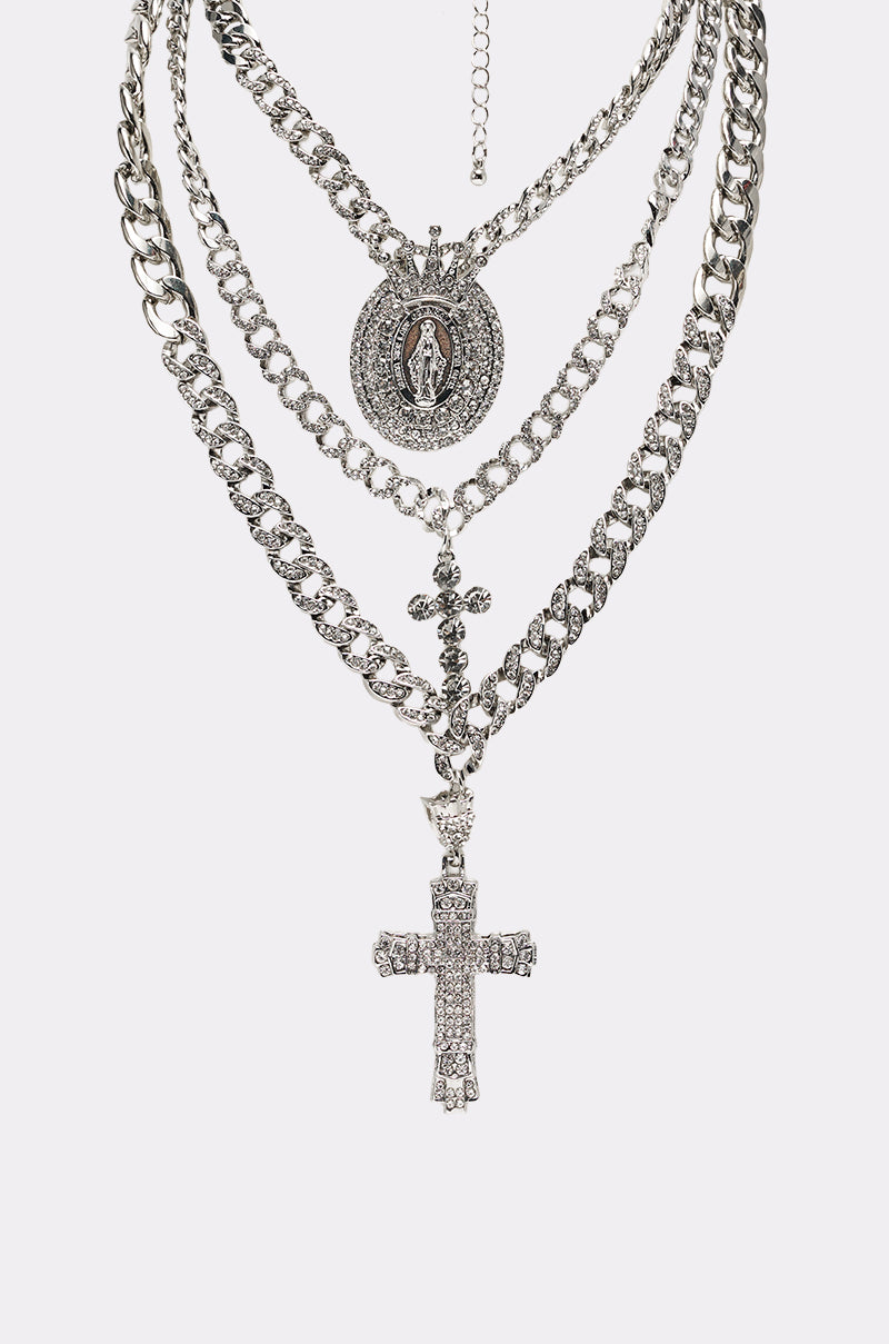The PRAY FOR YOU NECKLACE SET includes four layered silver chains: one with a large cross, one with an engraved Virgin Mary pendant, and two simple chain links adorned with shiny rhinestones. 3