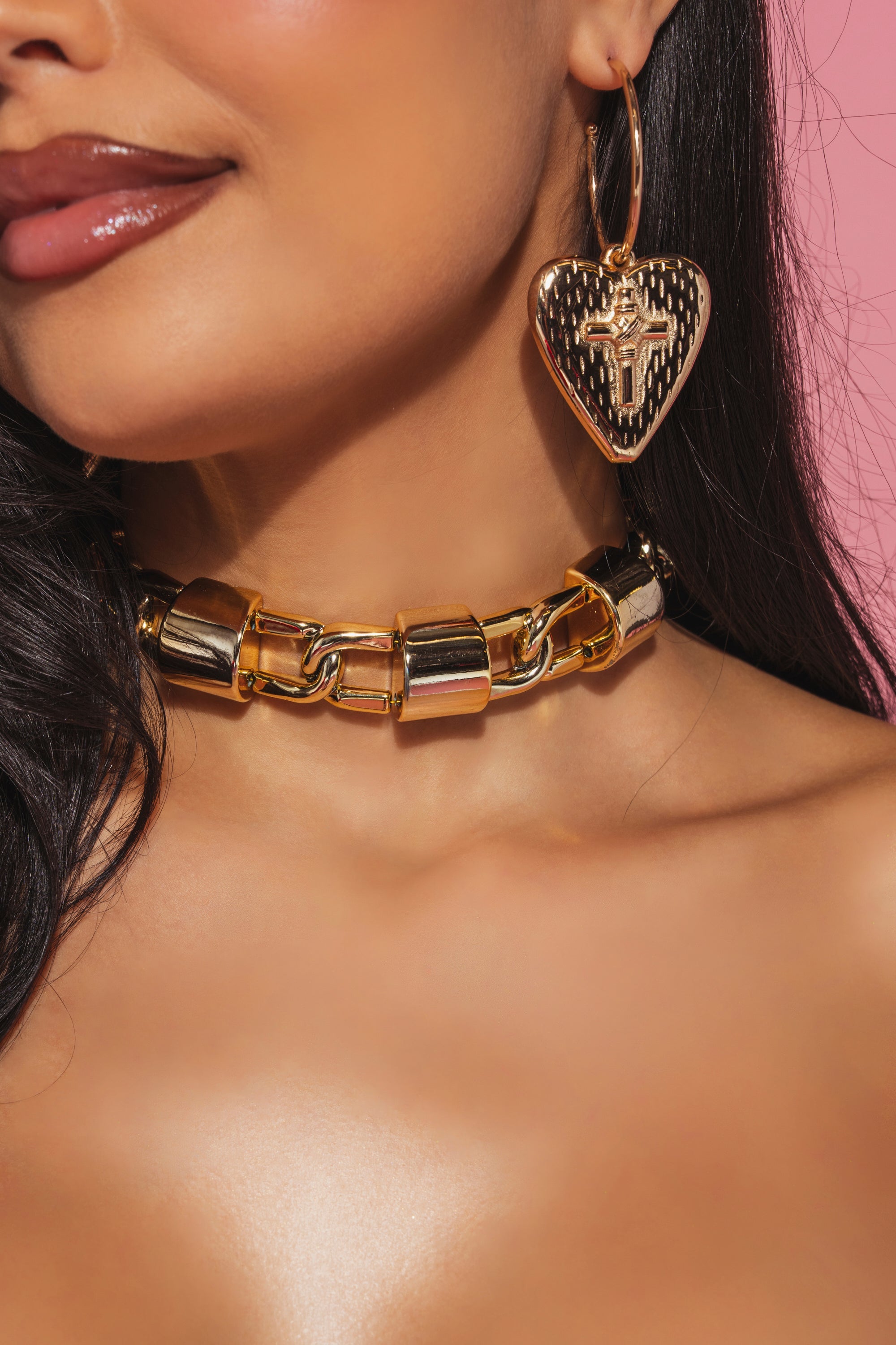 Close-up of a woman wearing the CHUNK CHAIN PLASTIC CHOKER and a large heart-shaped earring with cross detail. Her glossy lips and long dark hair pop against a pink background, accentuating the bold, oversized chain style. 0