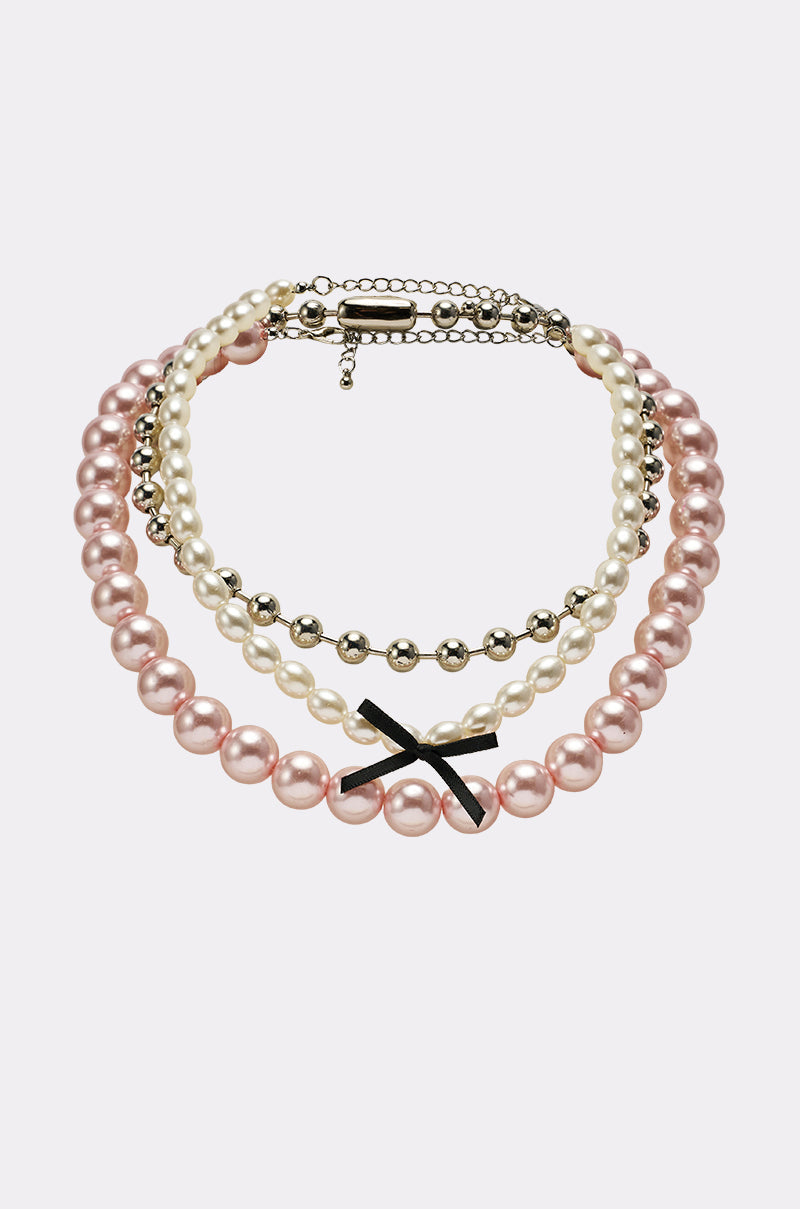 The GWEN NECKLACE SET features layered strands of blush pink pearls, white pearls, and silver beads, accented with a black bow and finished with an adjustable clasp. 0
