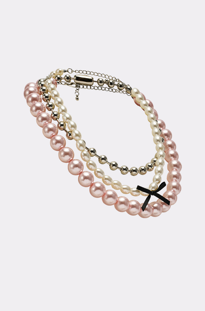 The GWEN NECKLACE SET features layered pink and white pearls, silver beads, and a black cross pendant—perfect for adding a feminine touch to any outfit. Displayed on a light background. 2
