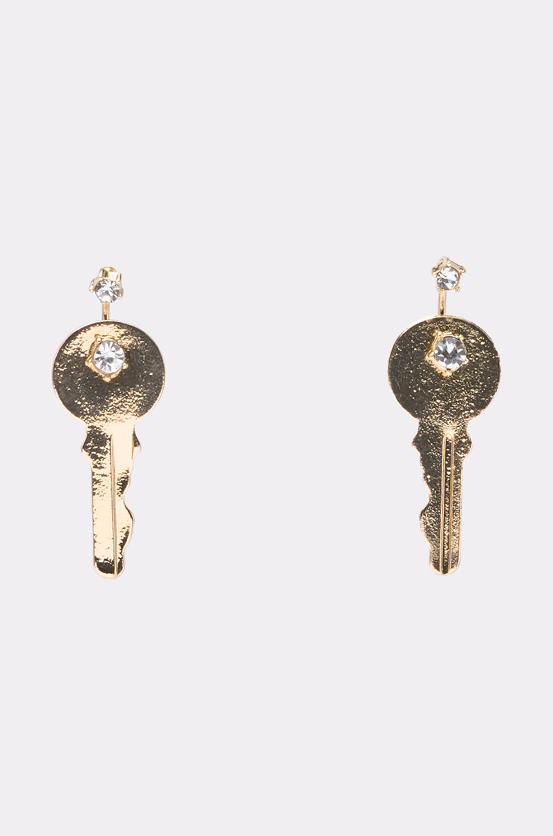 The I AM THE KEY EARRING features gold-tone key-shaped dangles, each adorned with a small clear gemstone at the top and another gem set in the head, shown against a plain light background. 0