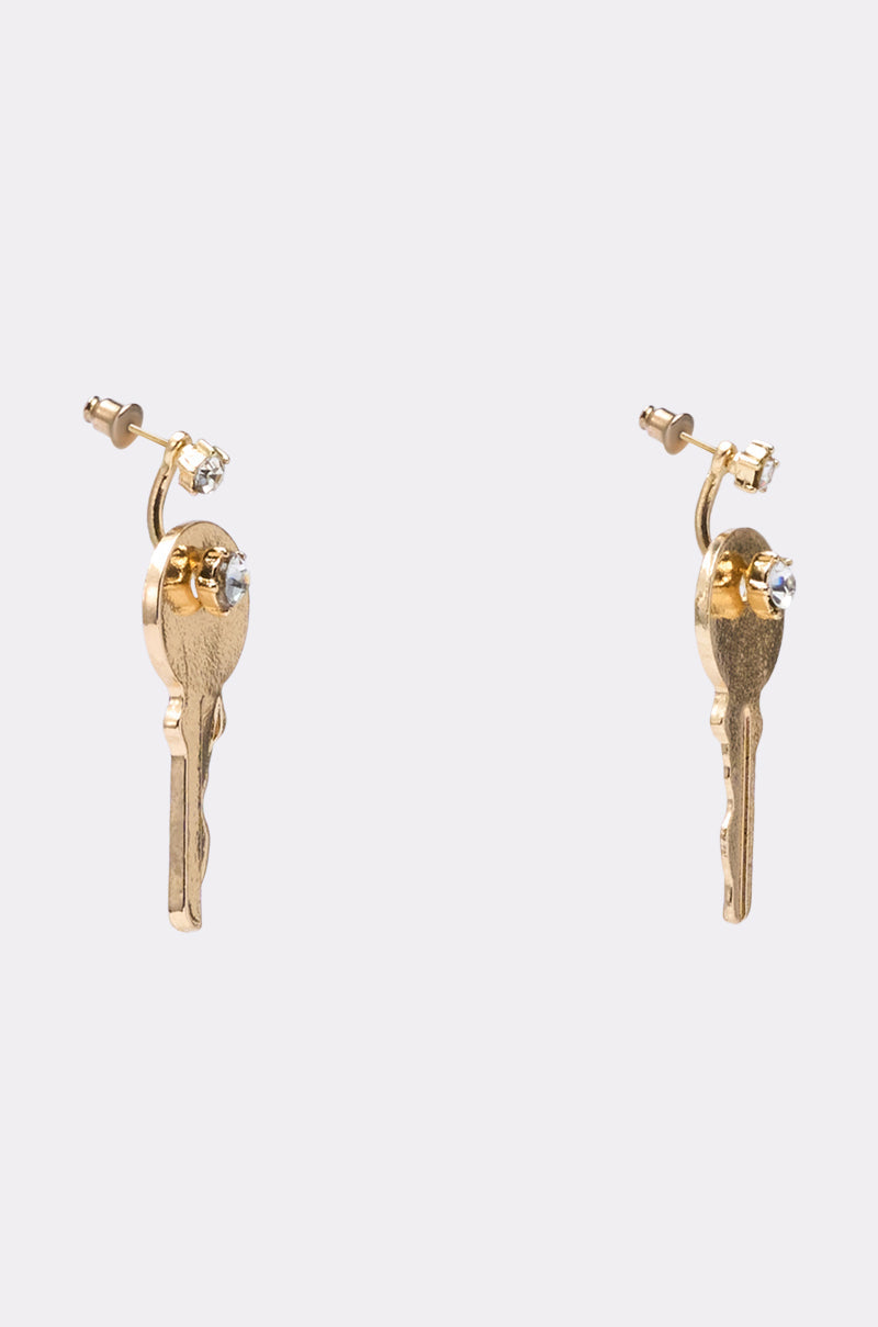 The I AM THE KEY EARRING features a pair of gold-tone key earrings, each accented with a small clear gemstone at the top, showcased against a plain light background. 2