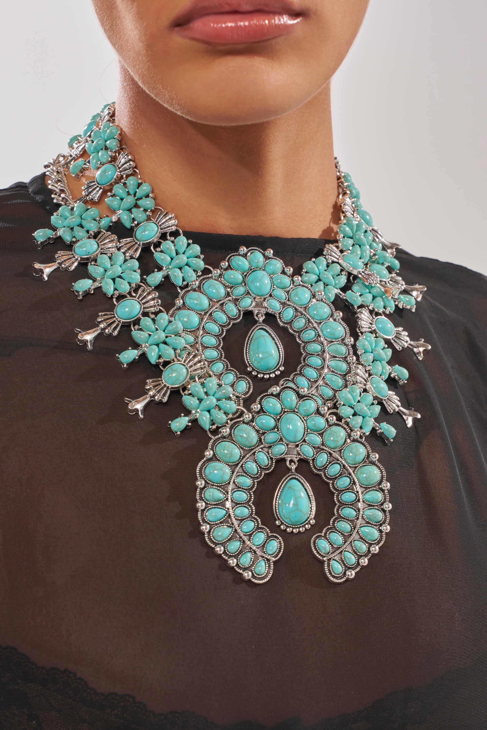 A person wearing a sheer black top and the HERE FOR THE VIBES NECKLACE, a bold boho-chic piece in turquoise with silver floral and geometric details. 2