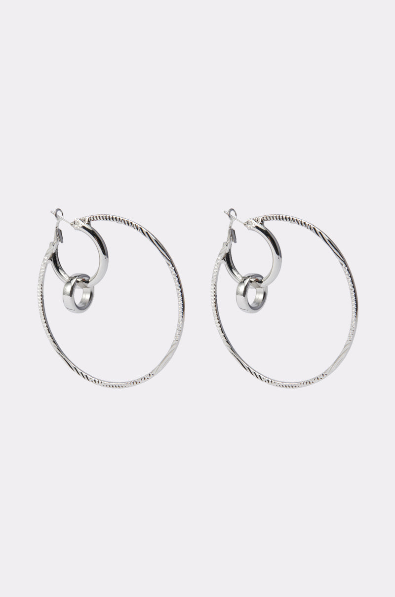 The TOO DIFFERENT HOOP IN SILVER features large silver hoops with a textured finish and two smooth interlocking hoops near the clasp, showcased on a plain light background. 2