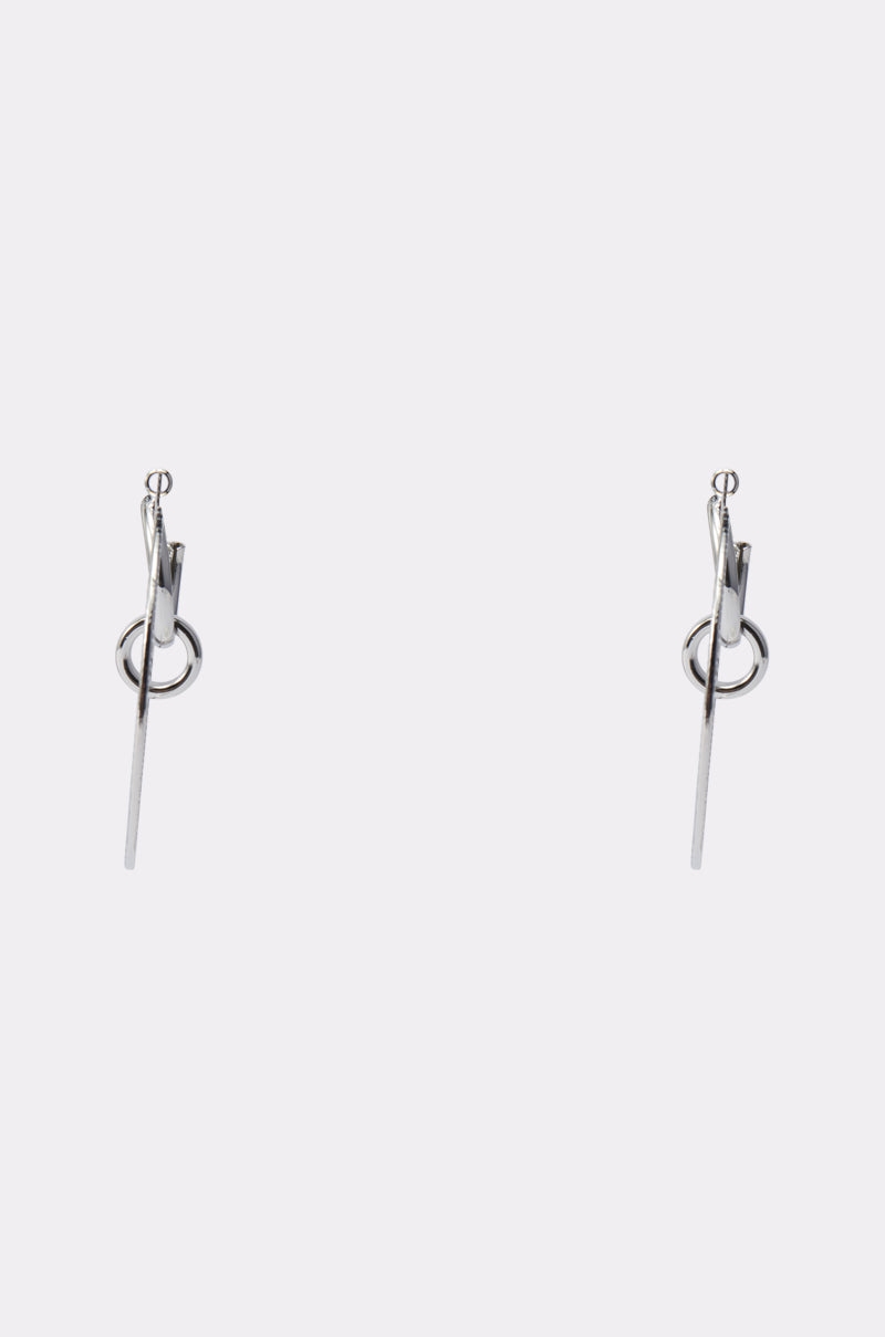 The TOO DIFFERENT HOOP IN SILVER is a minimalist pair of silver hoop earrings, each featuring a small hoop with a thin vertical bar dangling through it, displayed on a plain light background. 4
