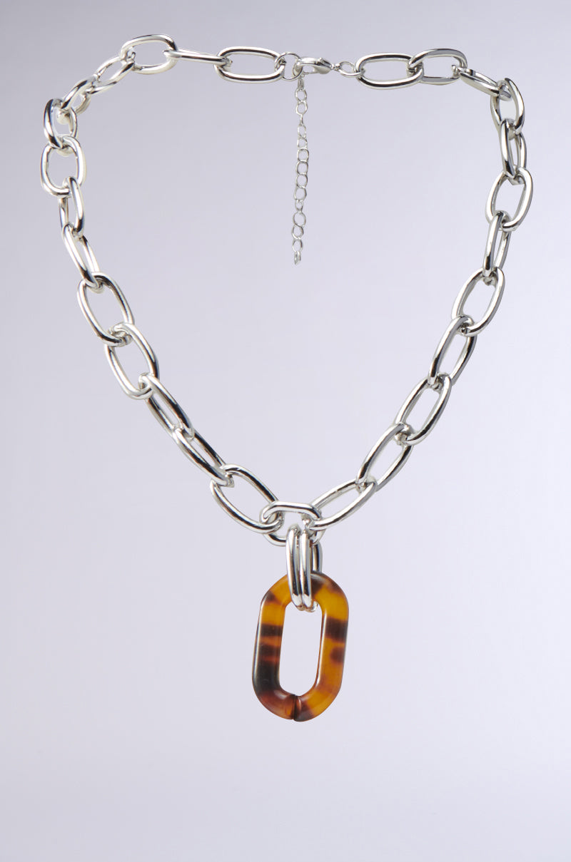 The MIXED FEELINGS NECKLACE features a chunky faux silver chain-link design with large oval links and an adjustable clasp. At its center, it boasts a striking tortoise shell pendant, blending modern and classic styles effortlessly.