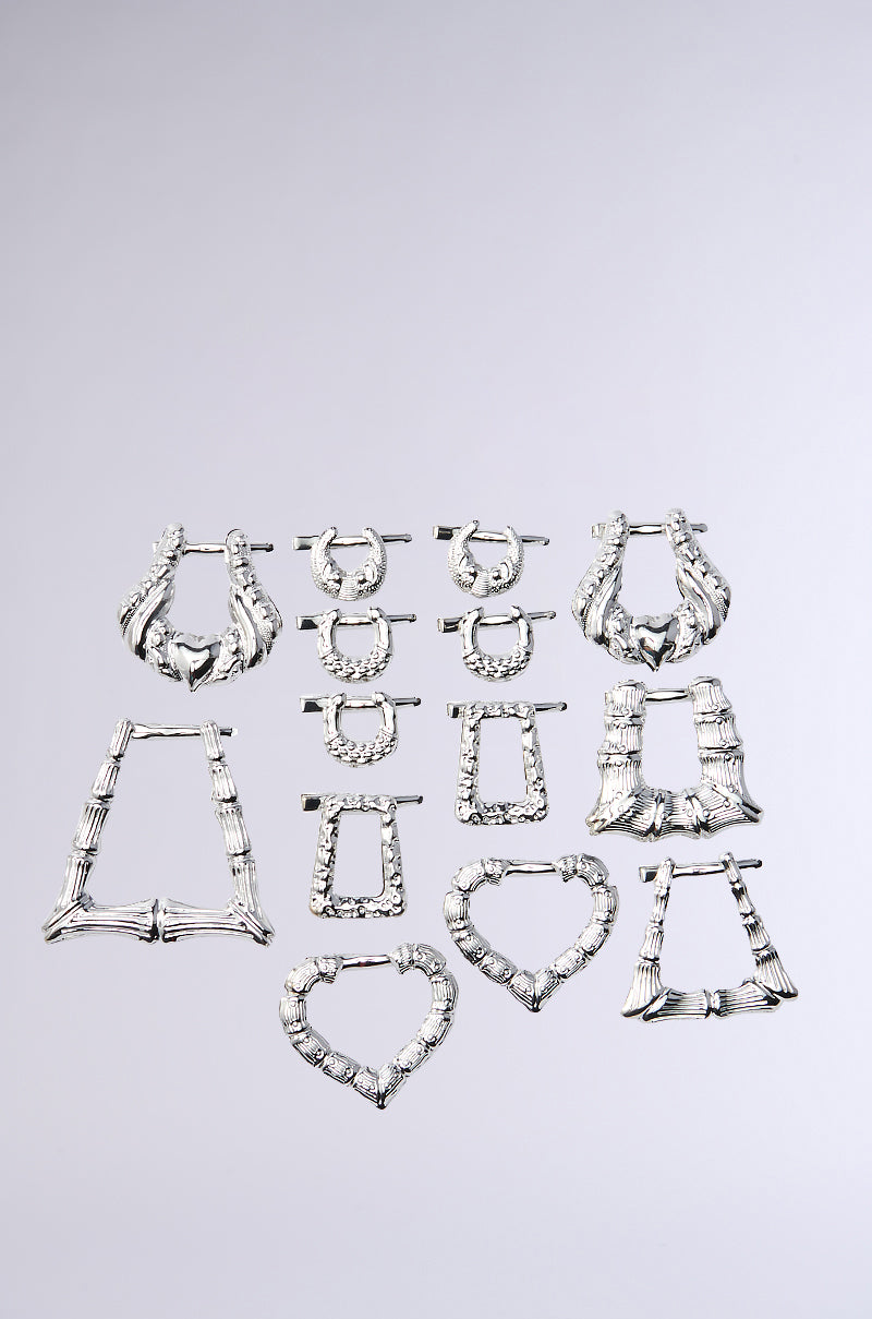 The I AM THE VIBE HAIR CLIP SET features nine silver hair clips in statement shapes—hoops, rectangles, squares, triangles, and hearts—arranged in three rows on a plain gray background. Each has a chunky texture perfect for bold hairstyles.