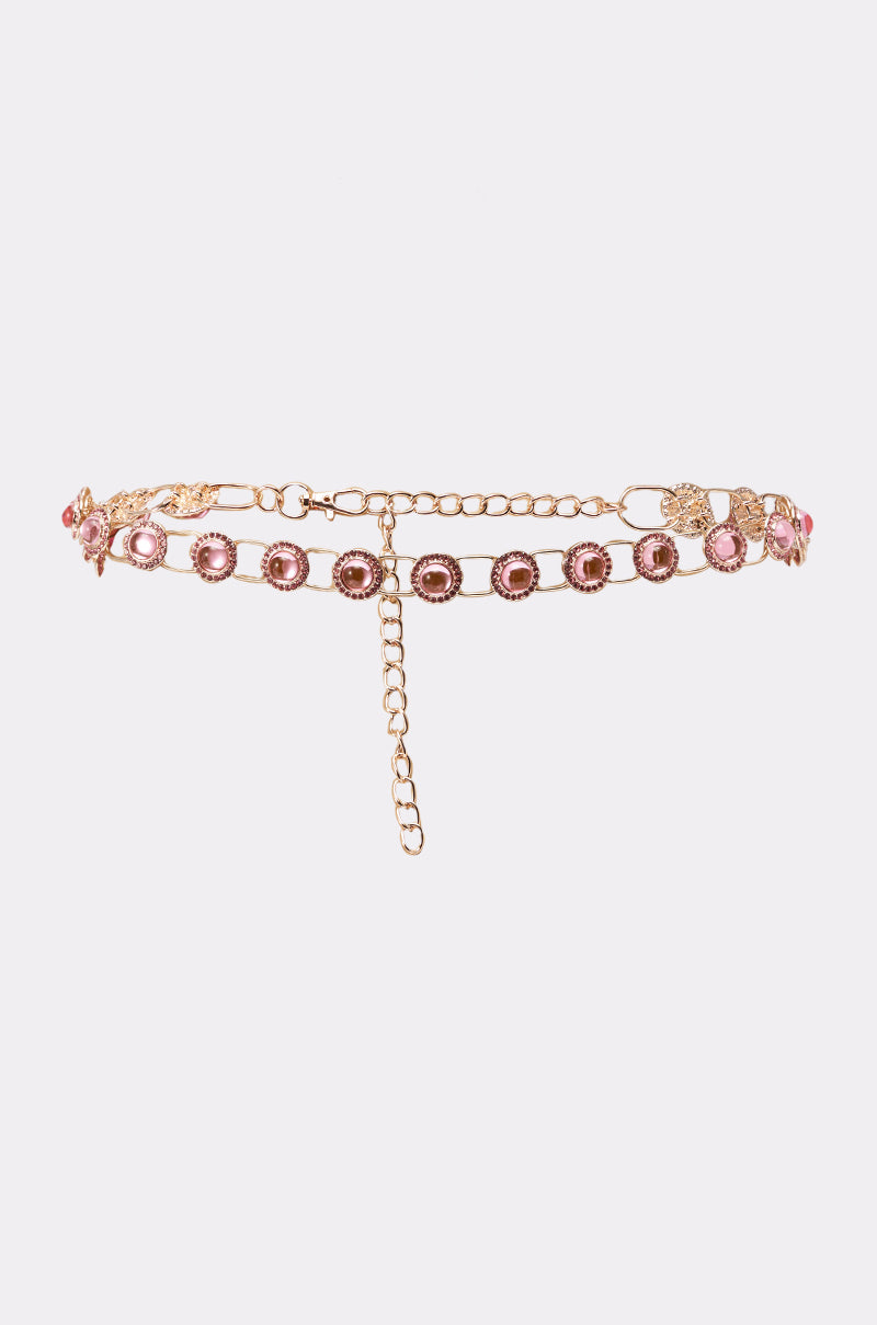 The ON A BOAT CHAIN BELT features a gold-tone chain with pink gemstones, floral clasp, and adjustable dangling chain. Delicate details make it a standout accessory, shown on a white background. 1