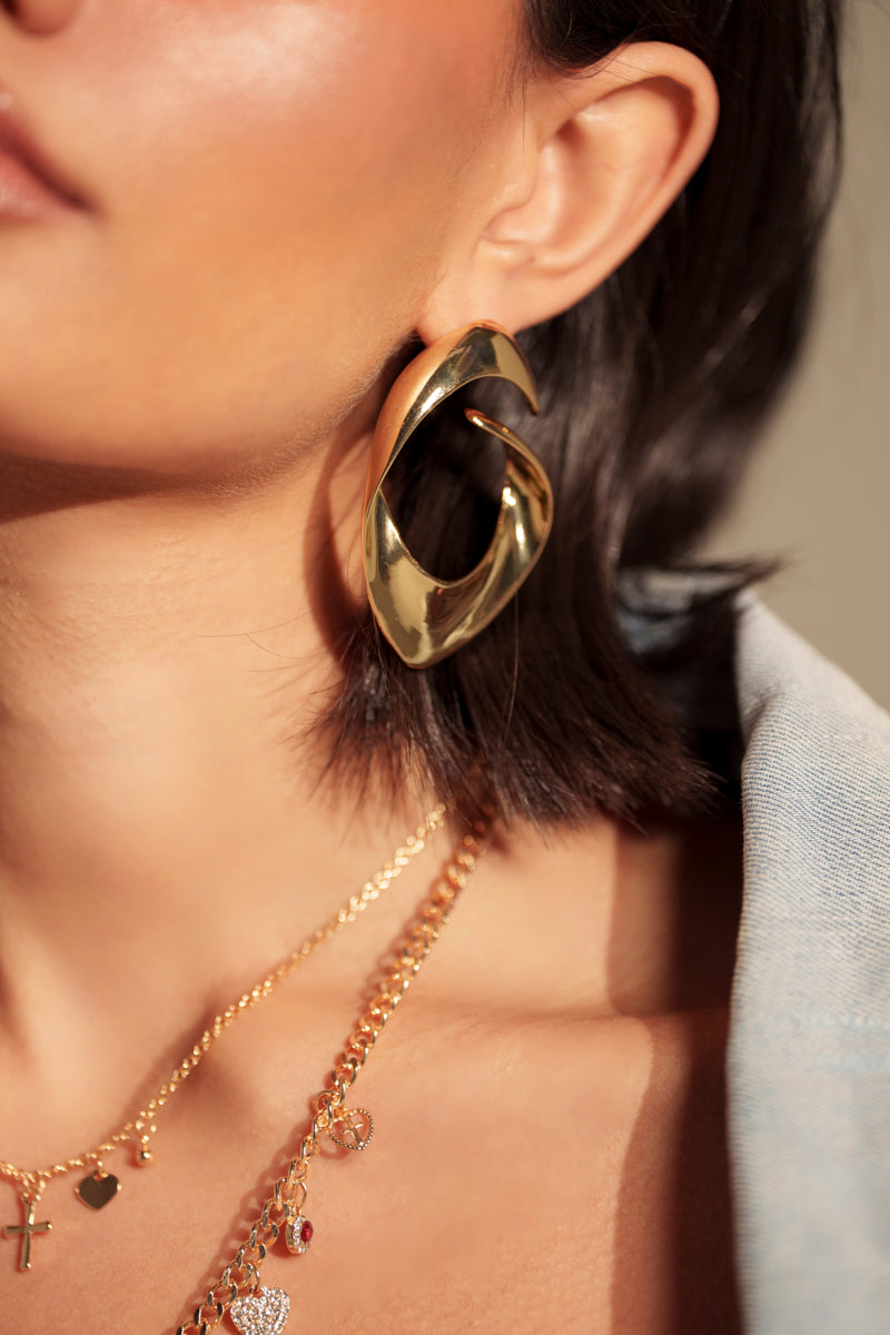 A close-up showcases the LOVERGIRL EARRING paired with layered gold metallic charm necklaces against bare shoulders and light blue fabric, creating a stunning, unforgettable date night look. 2