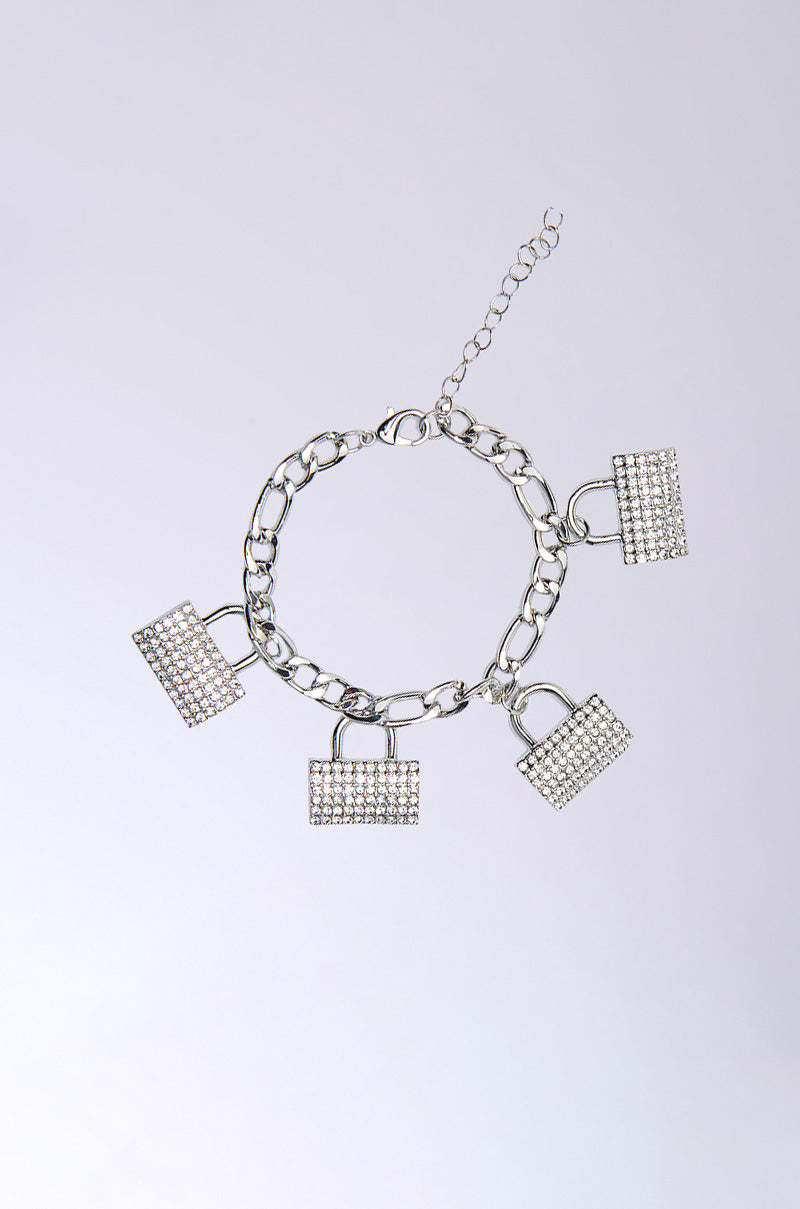 The GET YOUR BAG BRACELET, a silver chain with four rhinestone lock charms and a secure lobster clasp, is showcased on a plain gradient background.