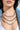 A woman wears the TAKE A NOTE SILVER NECKLACE layered with other chunky chains, beaded necklaces, large hoop earrings, a white top, and a blue denim jacket. Her lips are glossy and a partial chest tattoo is visible.