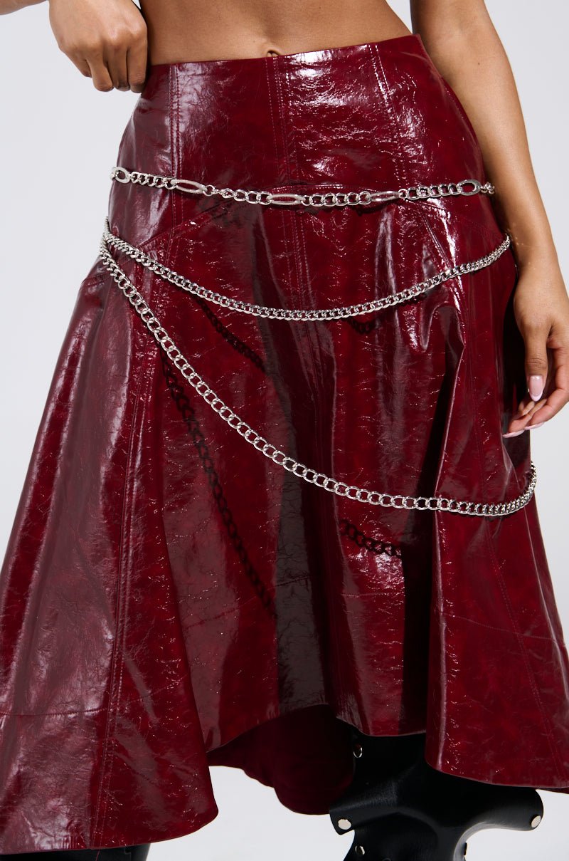 A person models a shiny dark red vinyl skirt with an asymmetrical hem, accessorized with the SILVER LINING CHAIN BELT featuring faux silver links and an adjustable lobster clasp. Only the lower torso and legs are shown.