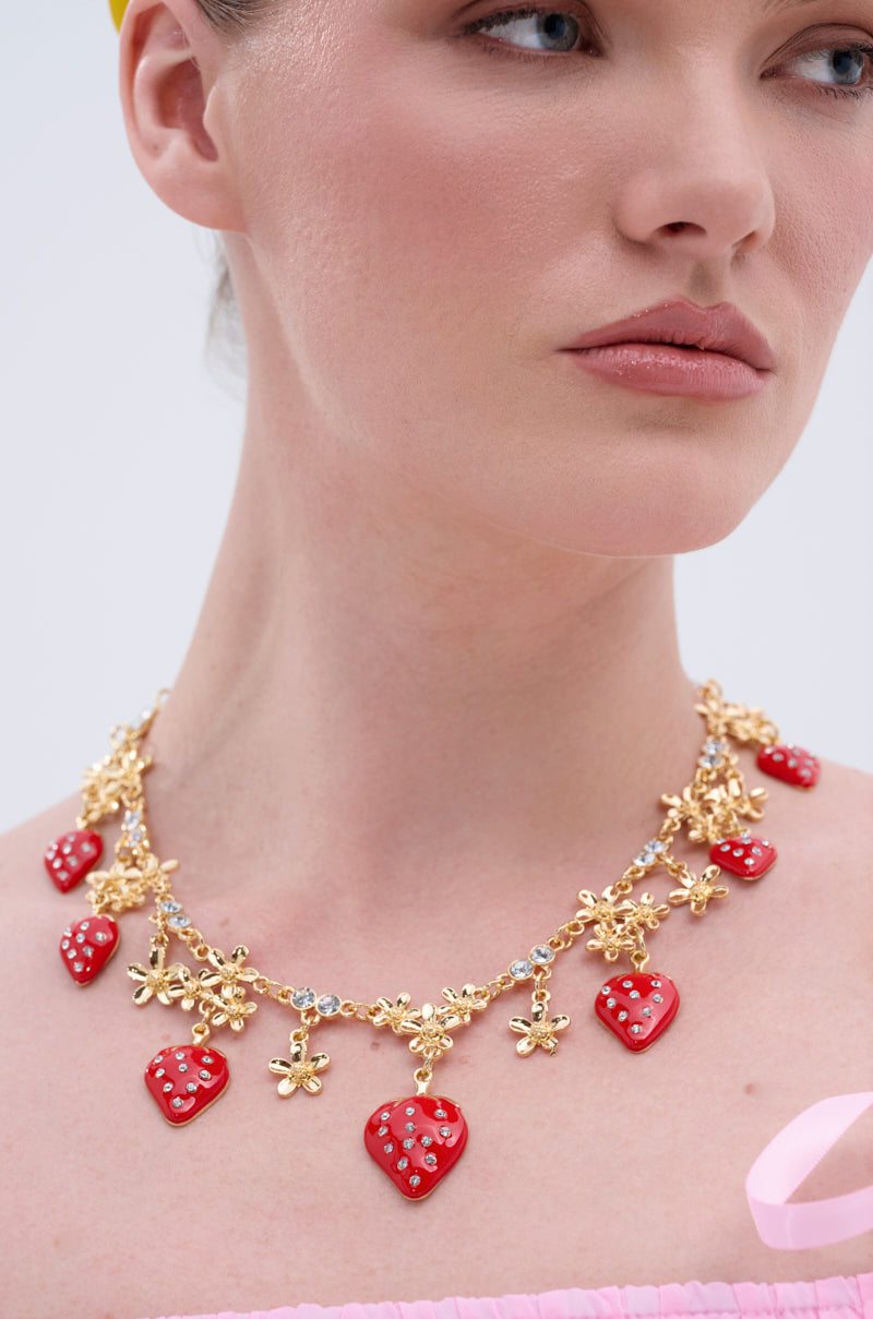 Wearing the PICK ME RED NECKLACE featuring rhinestones, red heart-shaped charms, and small gold flowers with a pink off-the-shoulder top—only the lower face and neck visible—makes this necklace the perfect summer accessory.