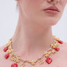 Wearing the PICK ME RED NECKLACE featuring rhinestones, red heart-shaped charms, and small gold flowers with a pink off-the-shoulder top—only the lower face and neck visible—makes this necklace the perfect summer accessory.