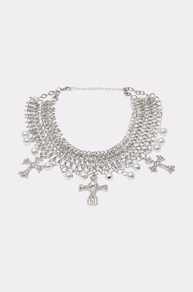 The CHARMED LIFE NECKLACE is a silver chainmail statement piece with large links, dangling pearl beads, and three rhinestone cross pendants, shown on a simple light background. 0