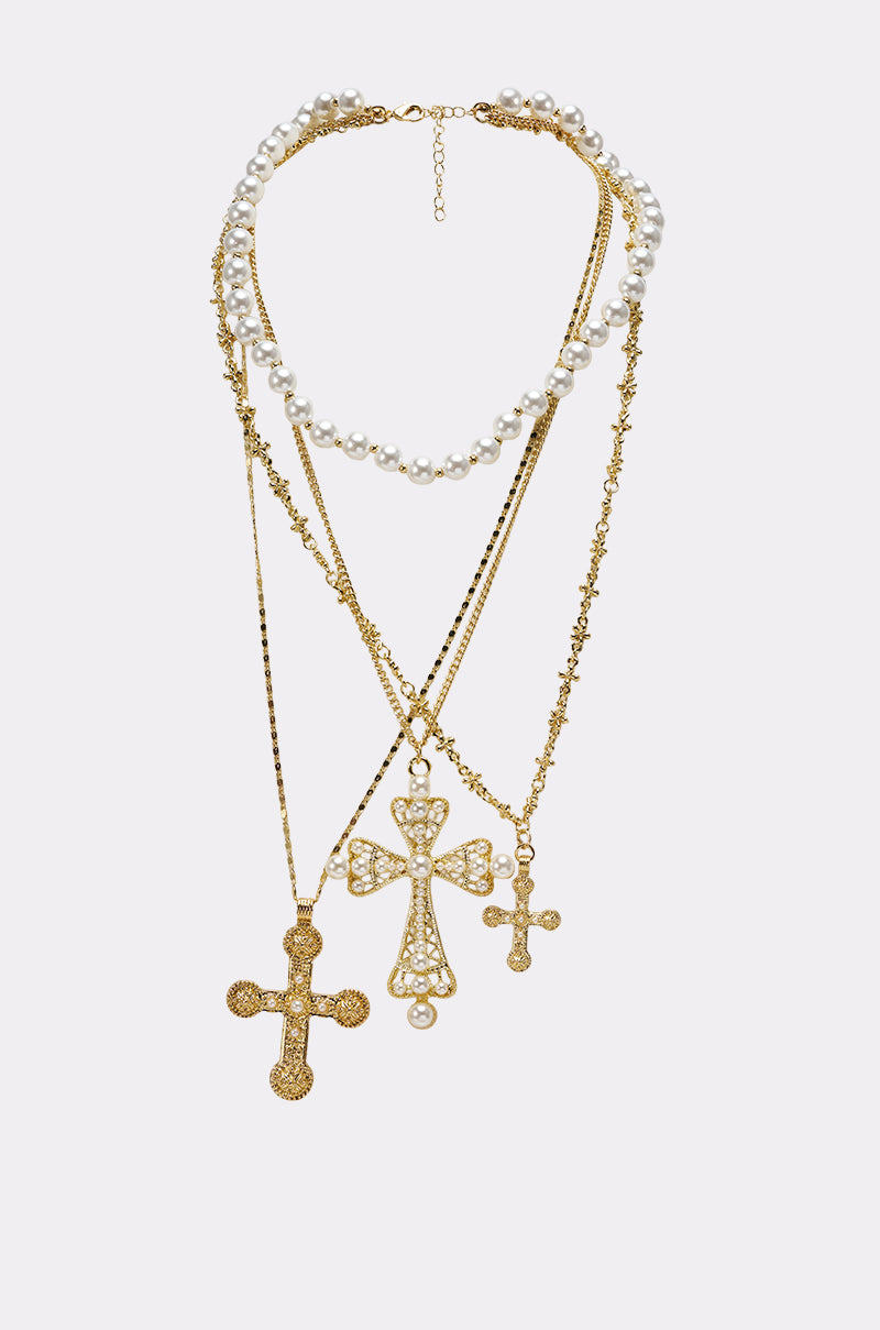 The SIERRA NECKLACE features layered gold chains, a pearl strand, and three ornate cross pendants in varying sizes, all showcased against a light background for a striking baroque look. 0