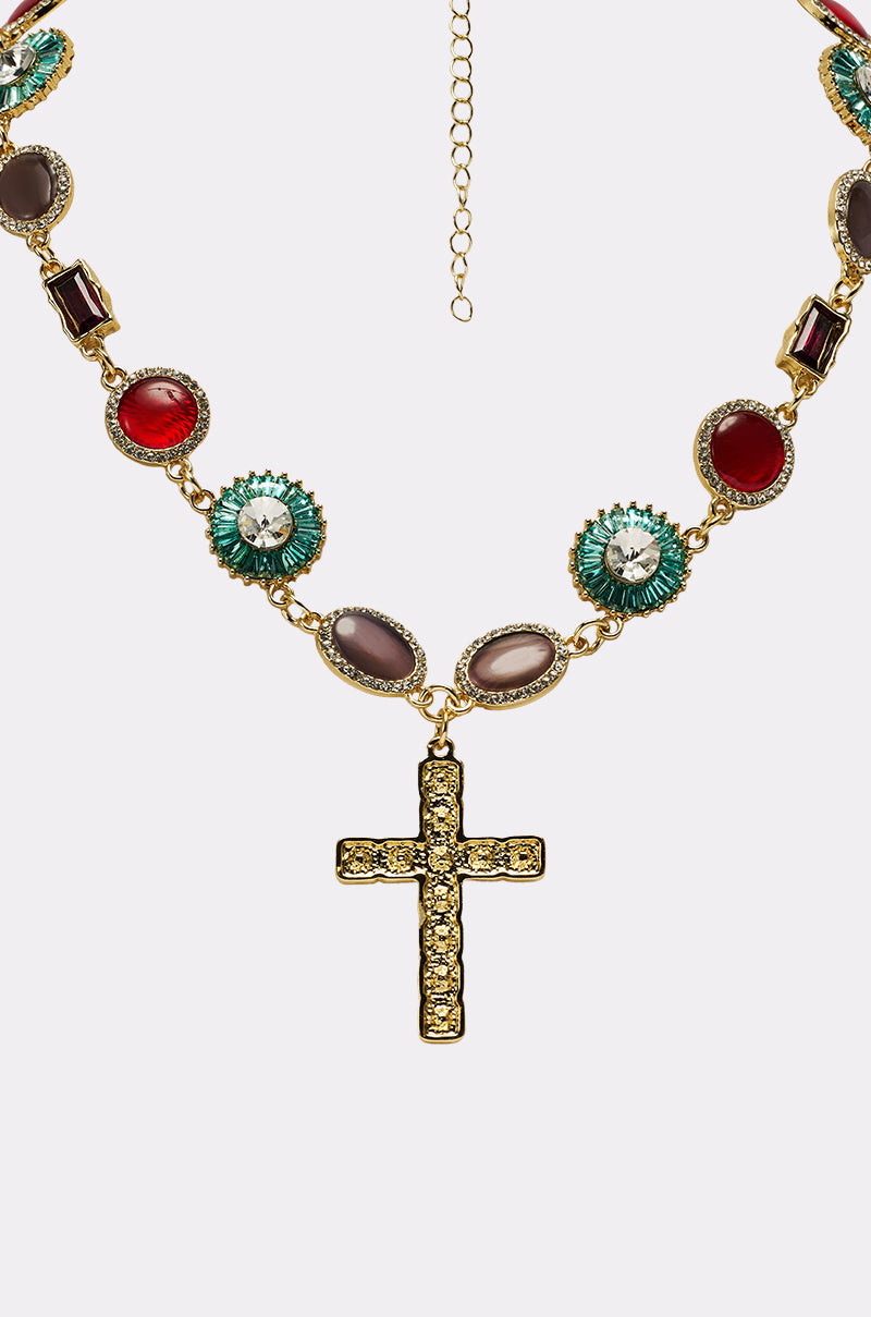 The LUXE TRINITY NECKLACE is a gold-tone piece with a jeweled cross pendant featuring alternating oval and round gemstones in red, green, and neutral shades, each framed by sparkling crystals. 5