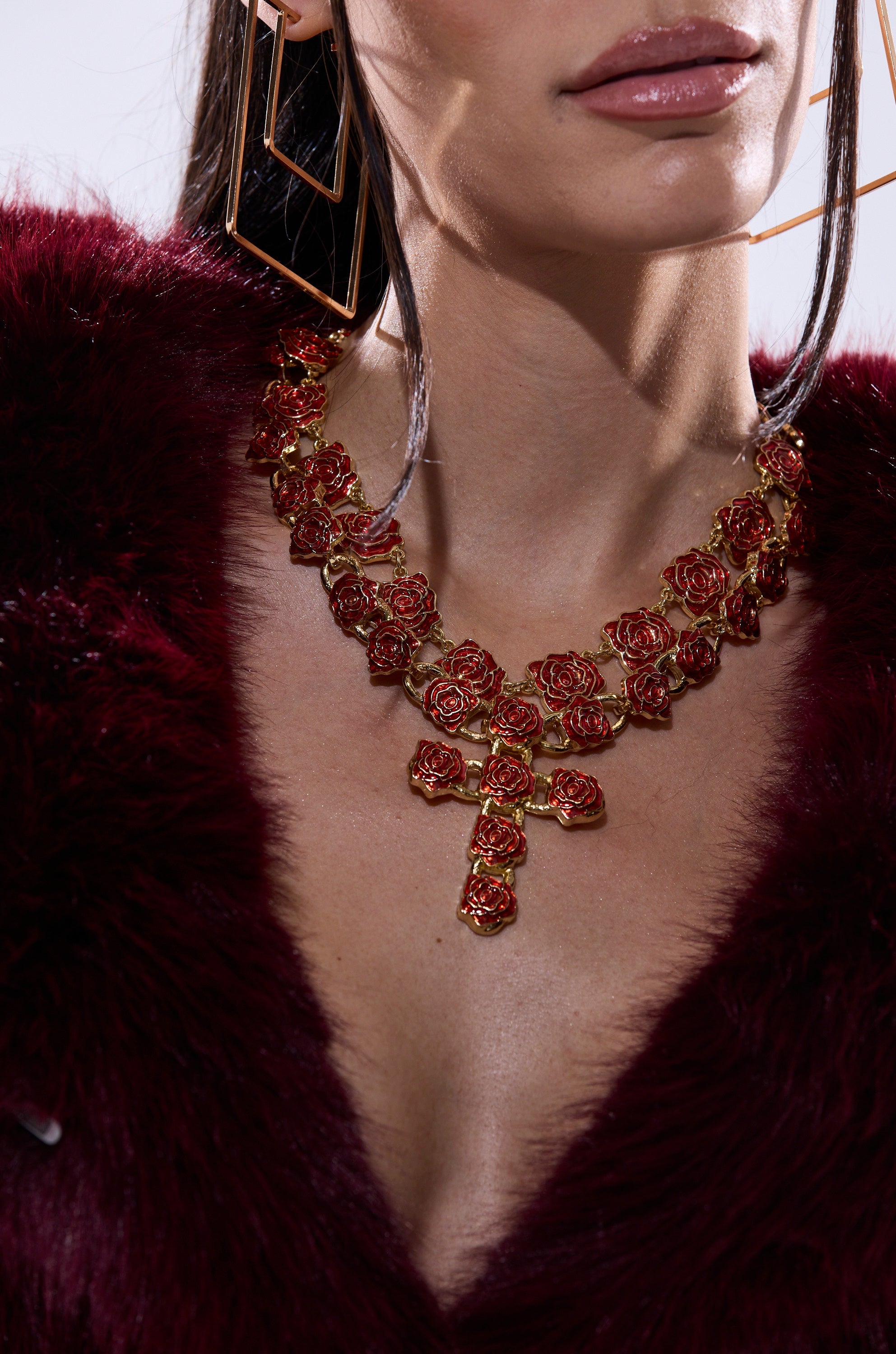 A woman wears a deep burgundy faux fur coat, the ROSES ARE RED NECKLACE SET with vintage rose details, and large geometric gold earrings. The image is cropped to show her lips, neck, and upper chest. 1