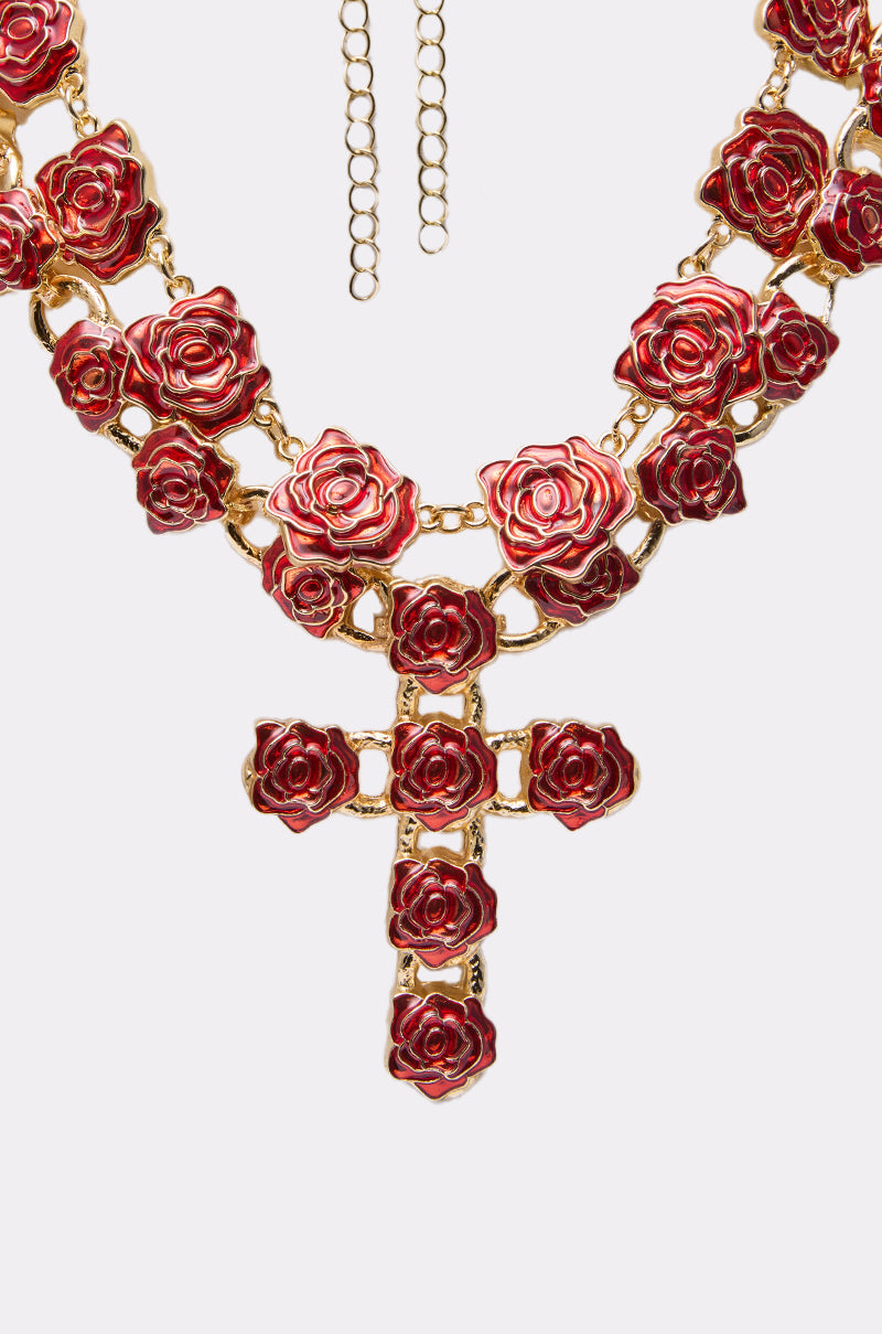 The ROSES ARE RED NECKLACE SET features gold-tone rose-shaped details and a bold cross pendant on an adjustable chain, elegantly displayed on a white surface. 2