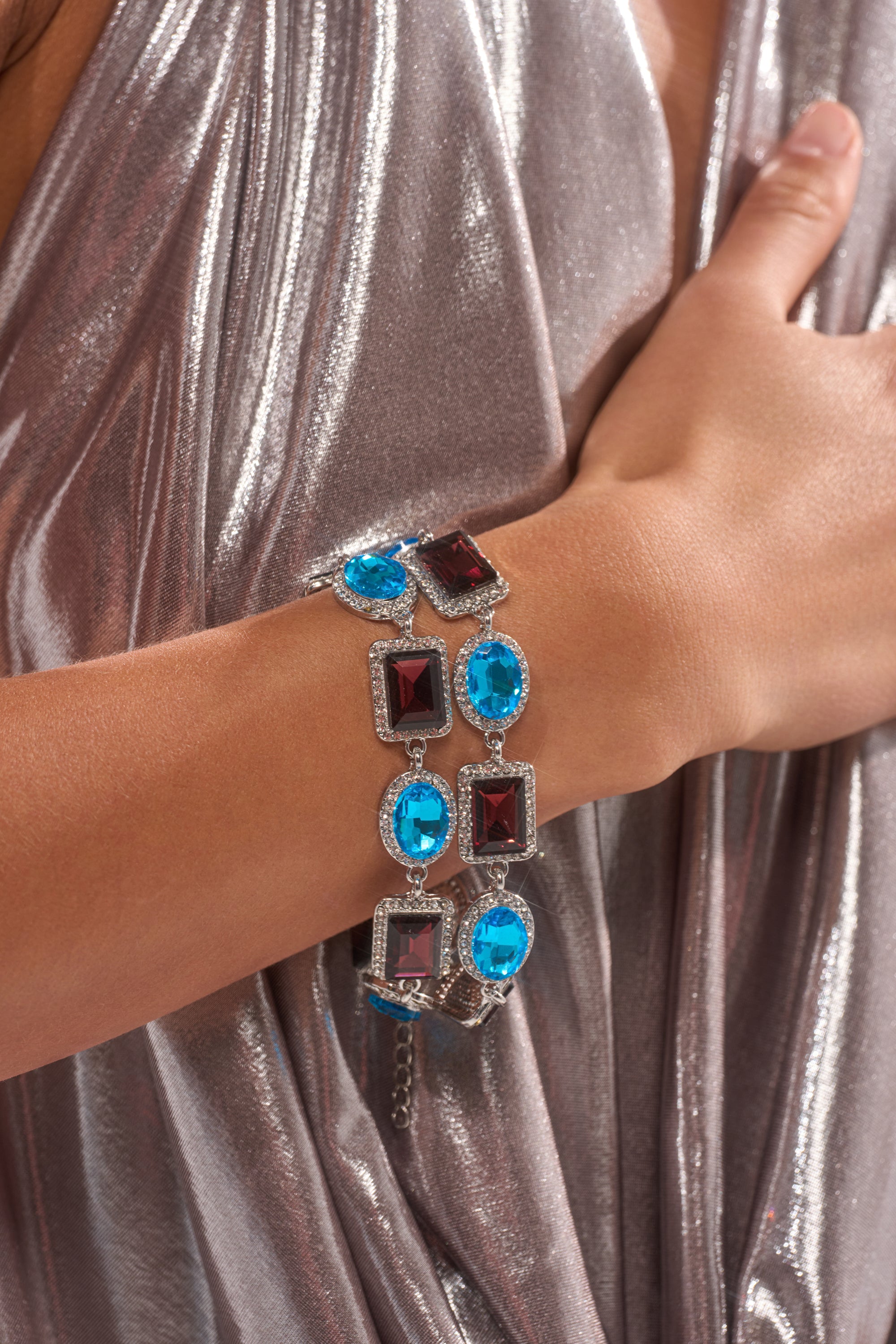 A person in a shiny silver dress displays the CHOCOLATE WONDER BRACELET SET, featuring an eye-catching silver chain with alternating large blue and red square and round gemstones.