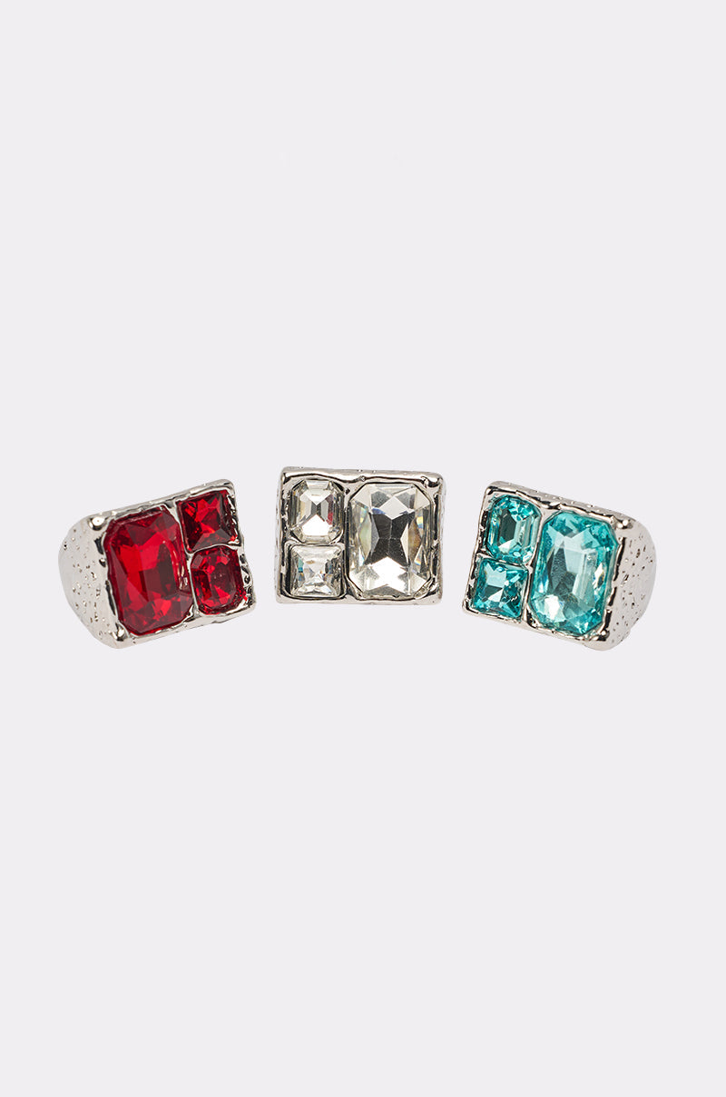 The FOR YOU RING SET includes three silver-tone rings with rectangular settings, each featuring bold geometric gemstones in red, clear, and blue, displayed against a plain white background. 0