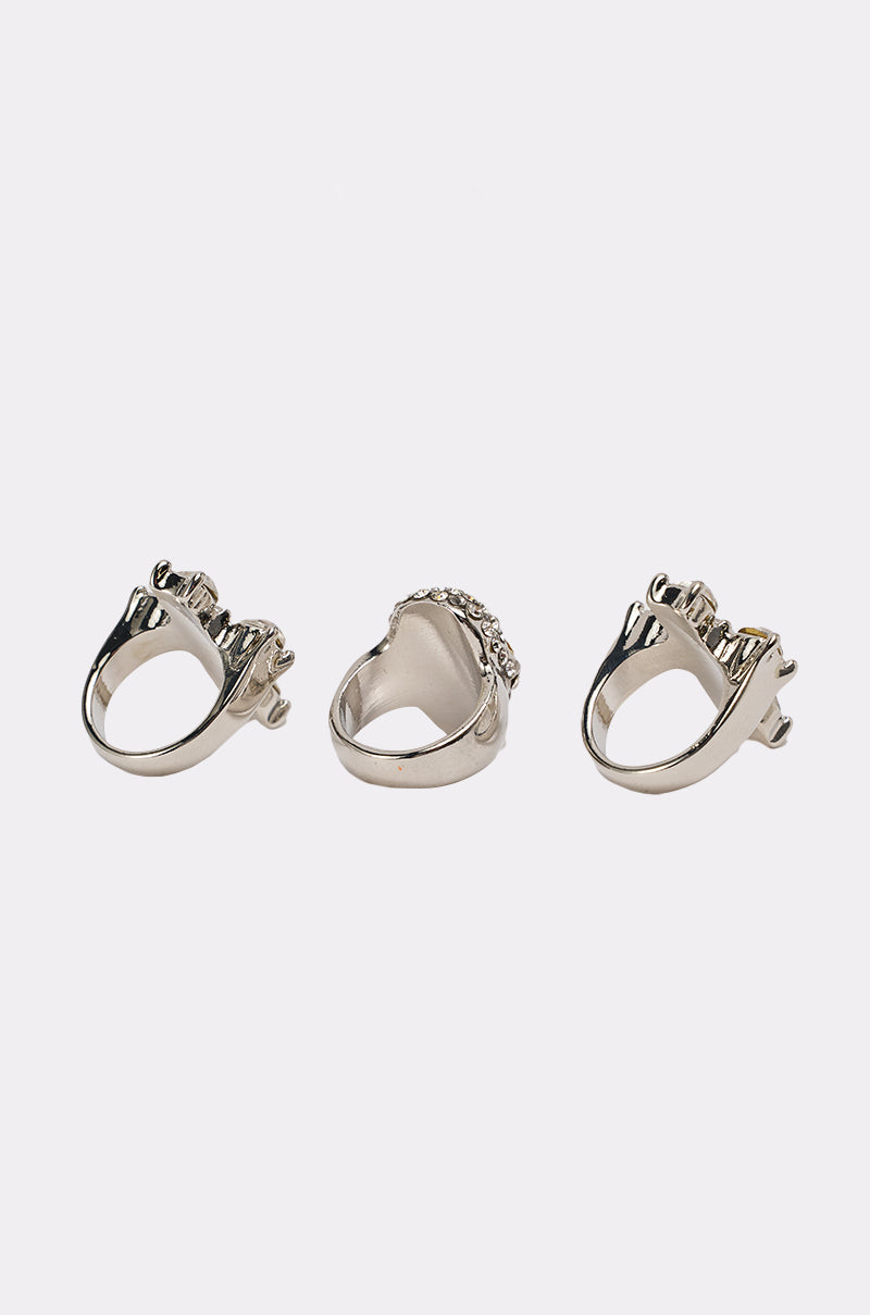 The FOREVER PROTECTED RING SET features three metallic rings, including a crystal-encrusted skull and crown-shaped designs, displayed on a plain white background to showcase their intricate details from various angles. 4
