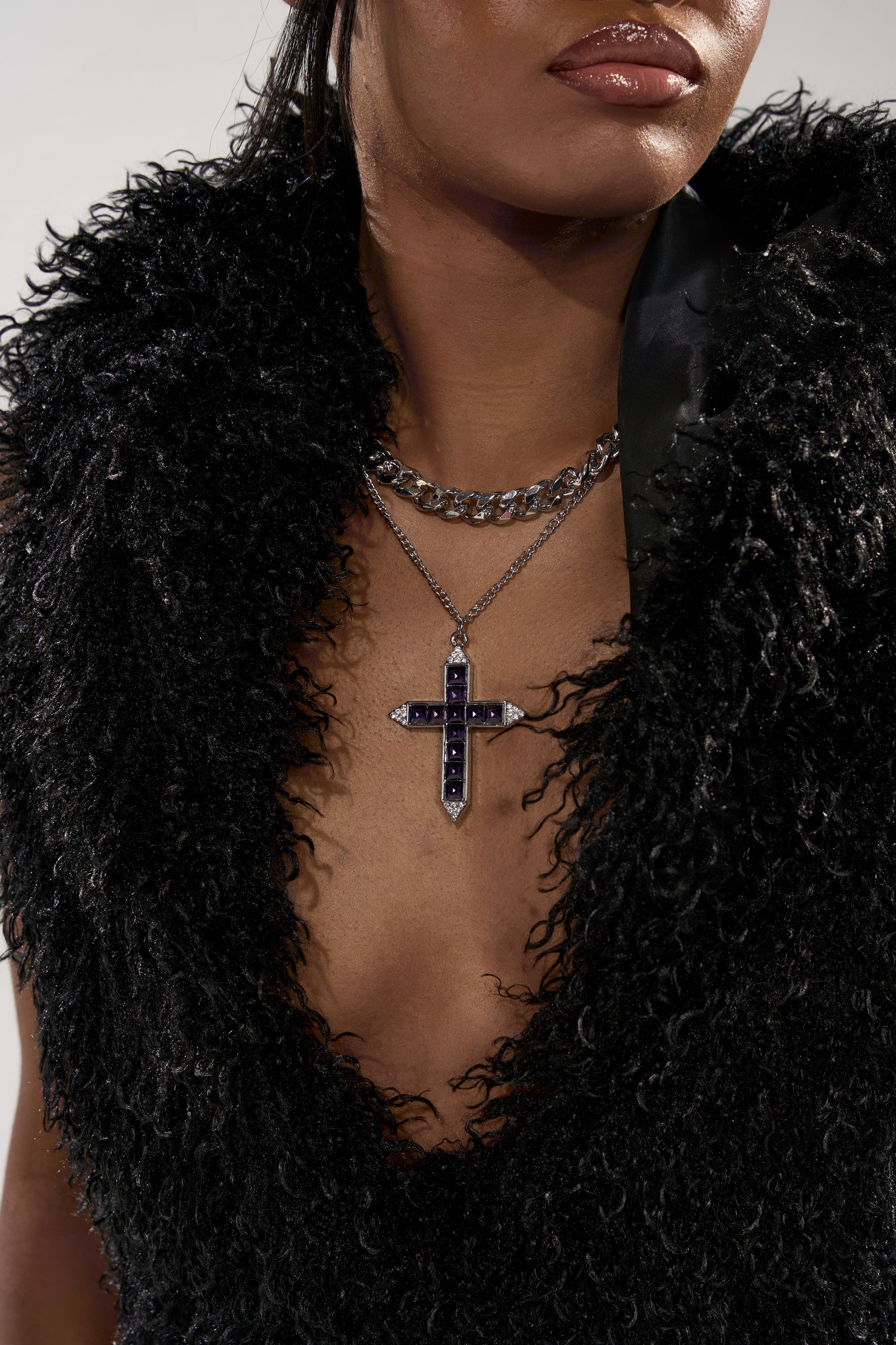 A person wears a textured black sleeveless top and layered necklaces, including the KIM NECKLACE—a chunky curb chain with a silver cross pendant adorned with dark stones. The image is cropped at the nose, showing only the lower face and neck. 1