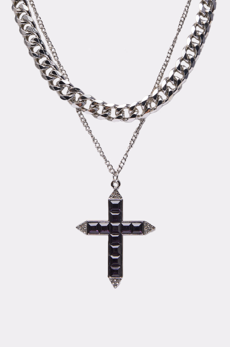 The KIM NECKLACE features two layered silver chains—a chunky curb and a finer chain—with a bold black gemstone cross pendant, creating a striking look against a plain white background. 2