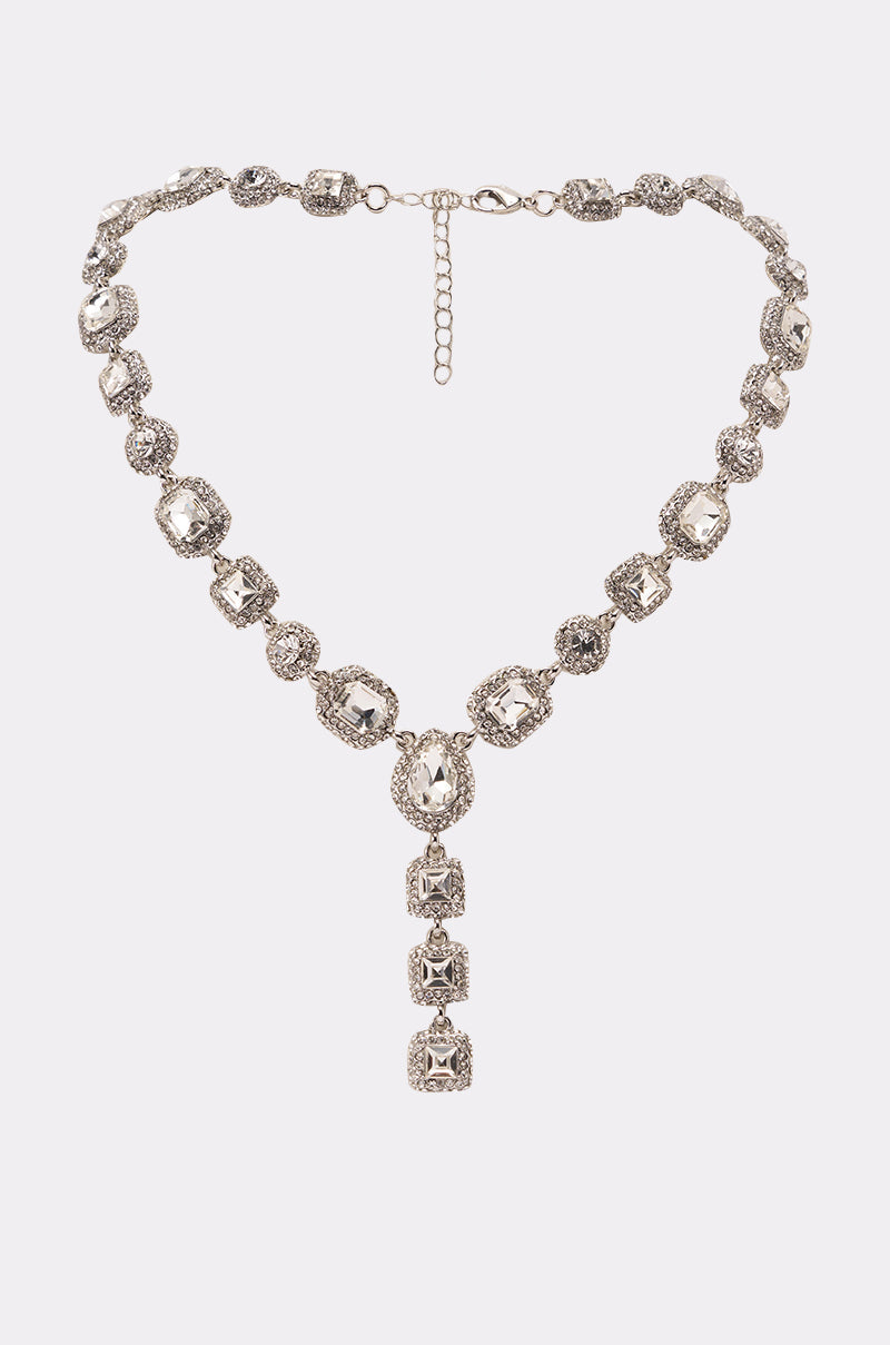 The LUXY LARIAT NECKLACE is a crystal-encrusted silver statement piece with alternating round and square gemstones, finished with a vertical pendant of four aligned square gems for an intricate, elegant touch. 0