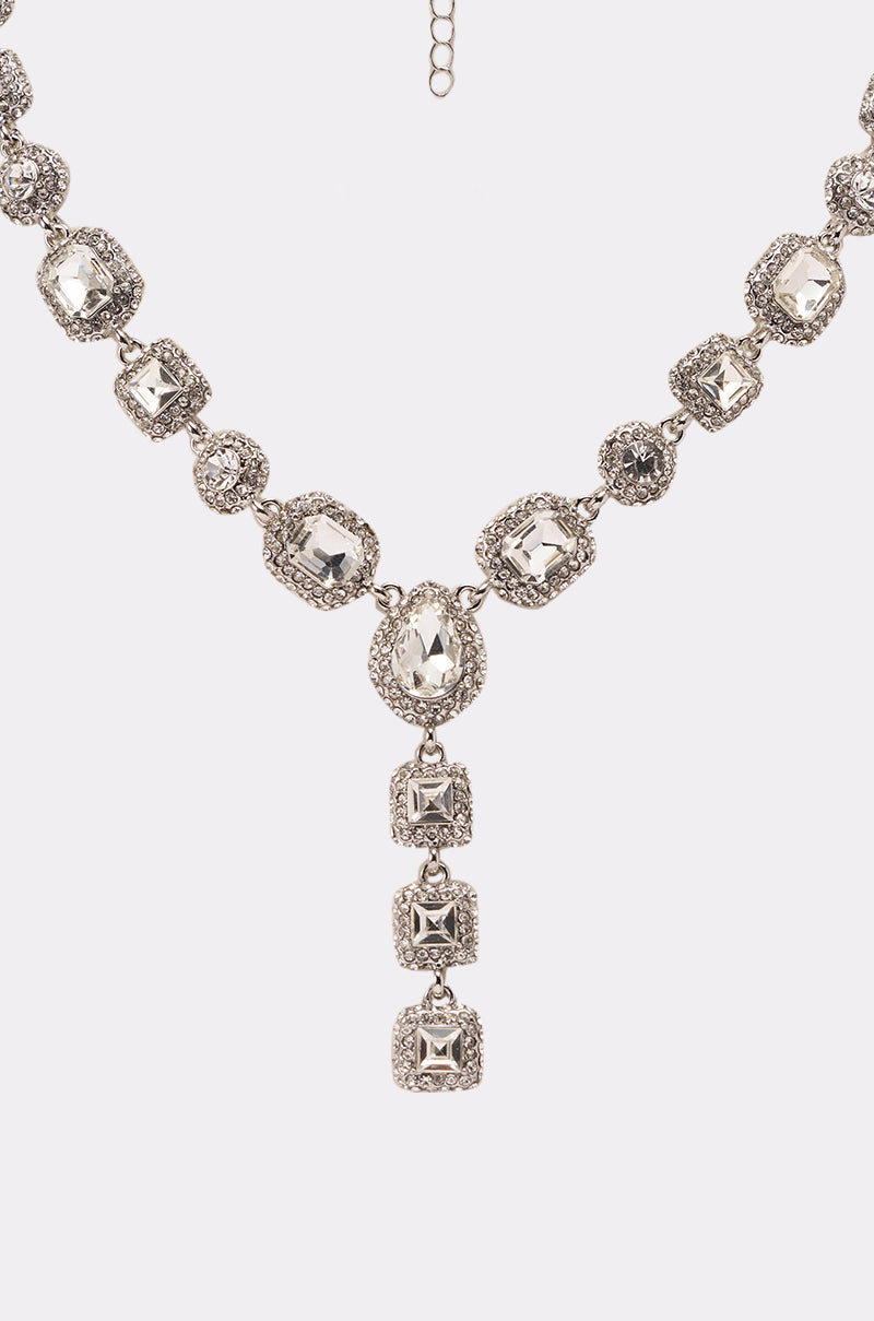 The LUXY LARIAT NECKLACE features large, clear gemstones in ornate square and round settings, highlighted by three square gems hanging vertically at the center. 2