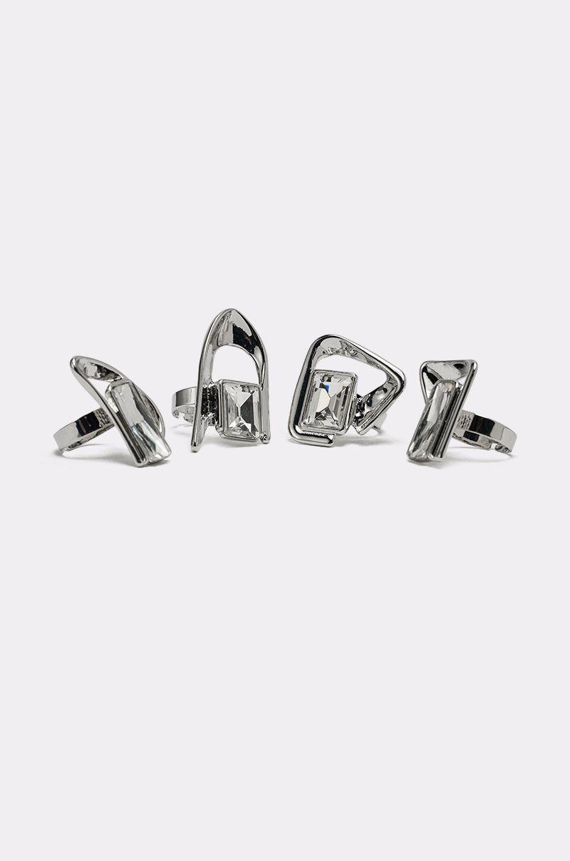 The TRUDY SILVER RING SET features four silver-tone rings, each with a unique geometric and sculptural design, displayed in a row on a plain white background. 3