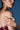 A woman wearing statement earrings and the DIRTY MARTINI RING SET poses with her hands on her bare shoulder, dressed in a burgundy lace-up top against a blue background.