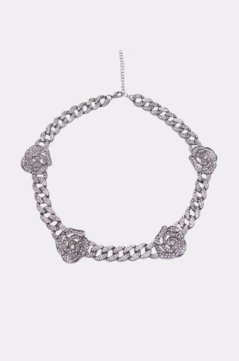 The FEELING ROSEY NECKLACE features four large, ornate rose-shaped rhinestone embellishments on a sleek silver chain, making it a stunning statement piece. Displayed on a plain white background. 0
