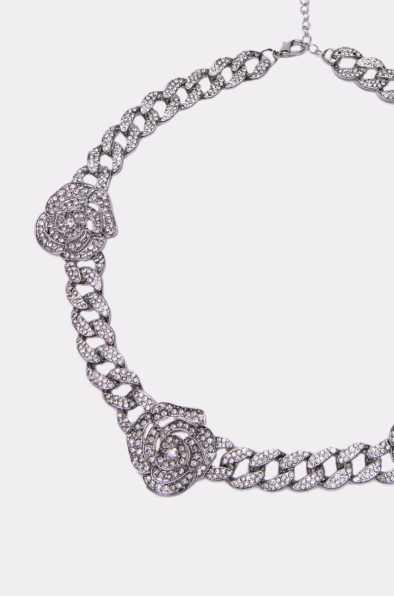 The FEELING ROSEY NECKLACE features a silver chain with three detailed rose designs, each accented by sparkling rhinestones, shown on a plain white background. 2