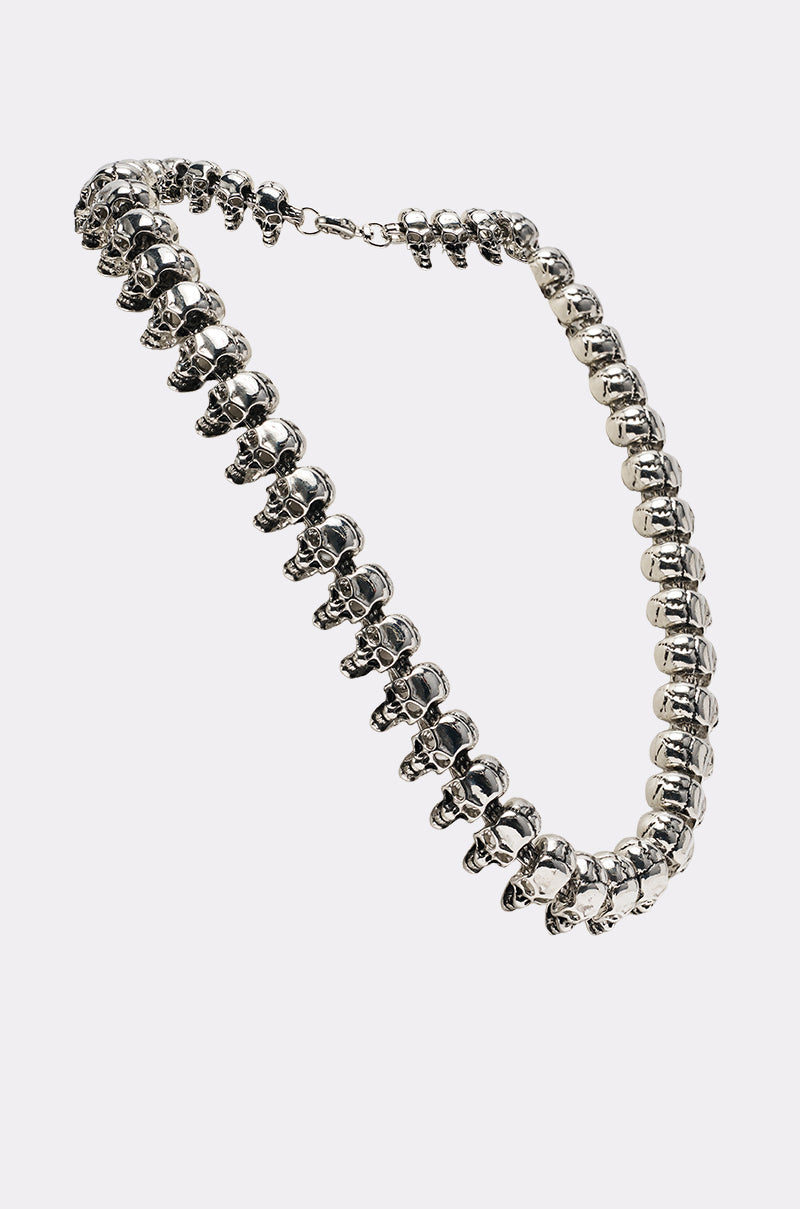 The SKULLY NECKLACE is a bold silver statement piece featuring linked metallic skulls in a continuous chain with a clasp, displayed against a plain light background. 4