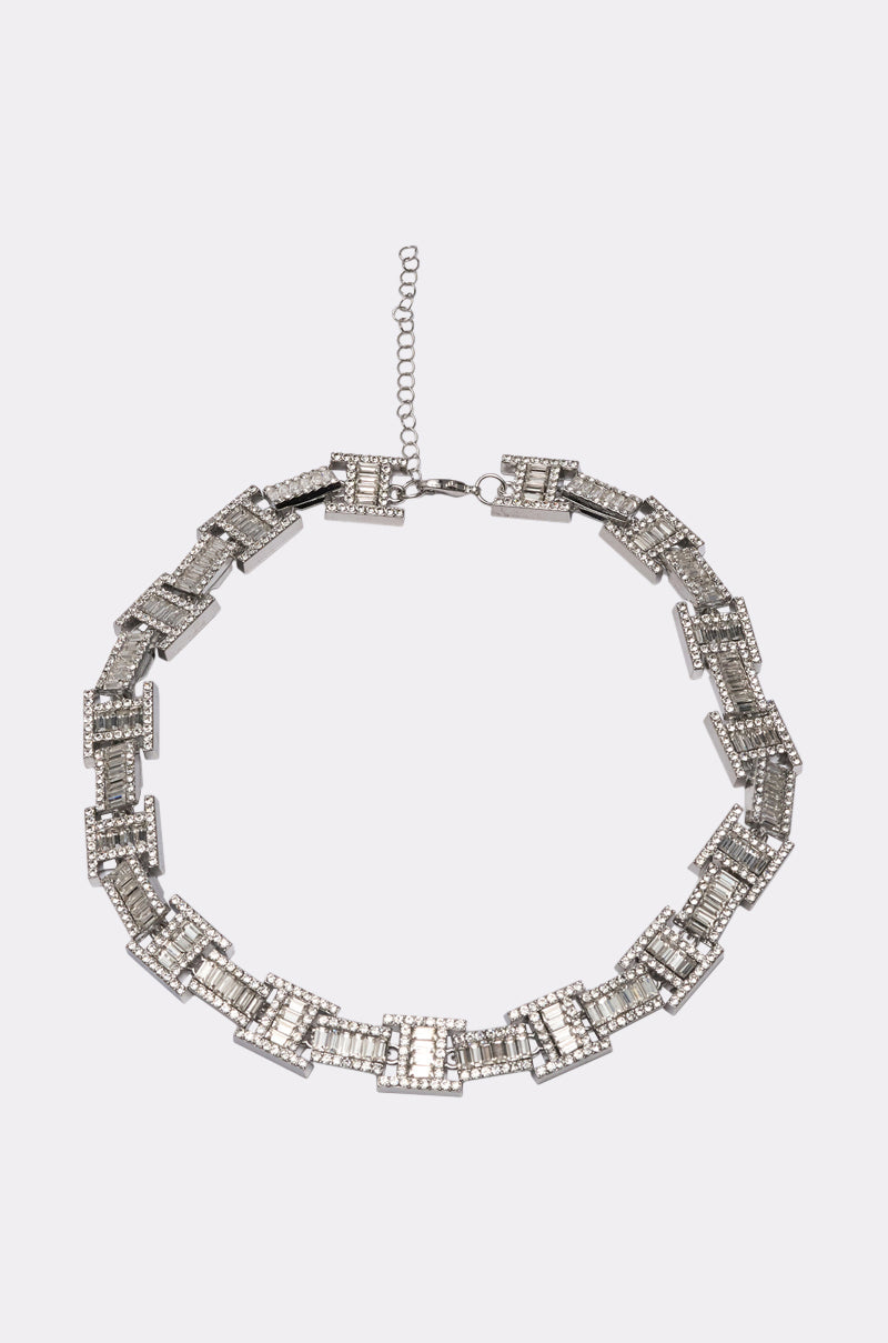 The LUXE ICY NECKLACE is a silver-tone statement piece featuring rectangular, baguette-cut crystal links with rhinestone accents in a chic chain pattern and an adjustable clasp, displayed on a plain light background. 3