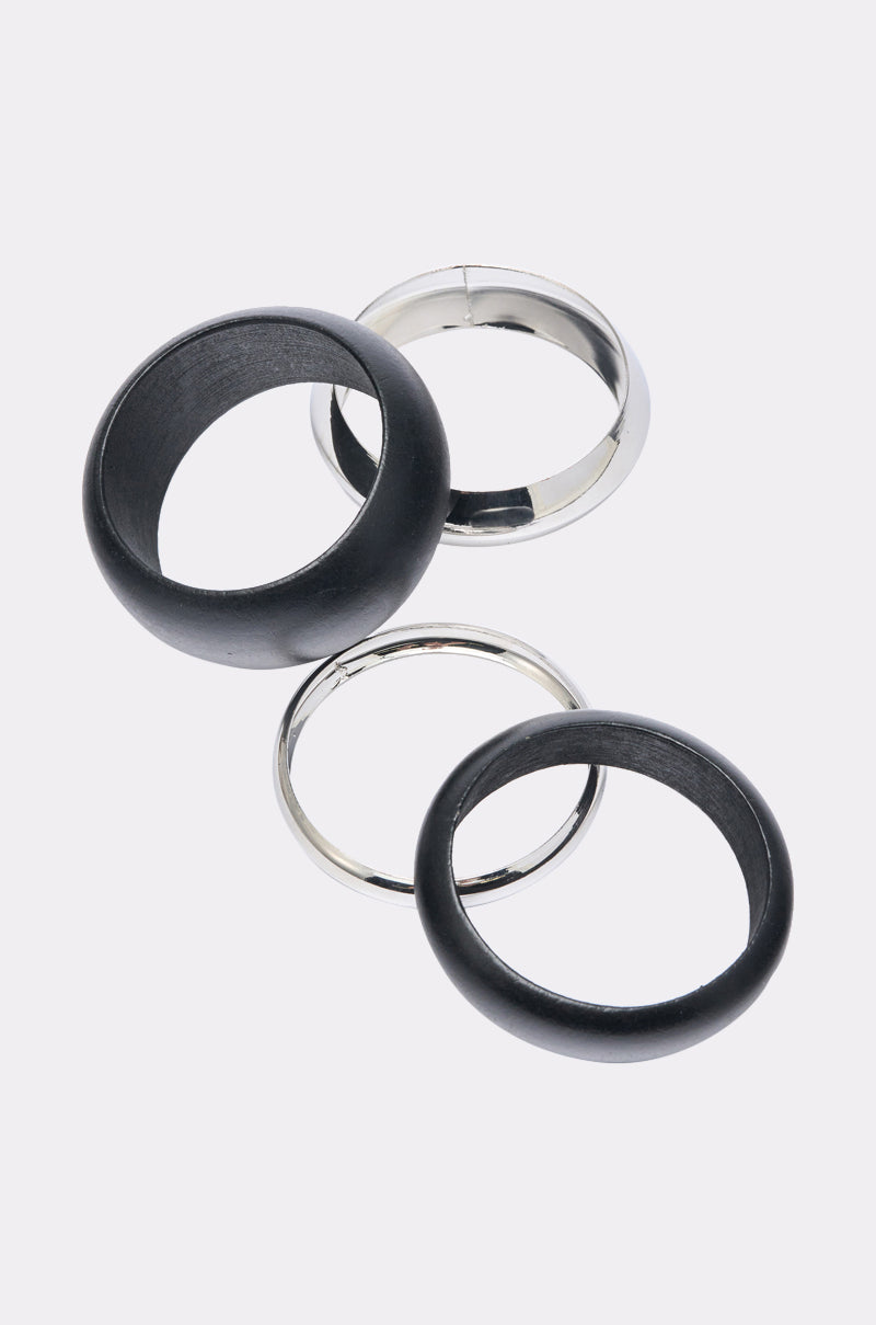 The MOD BRACELET SET, featuring two silver-tone bracelets and two black bangles, is displayed overlapping on a light gray background for a balanced, modern look. 1