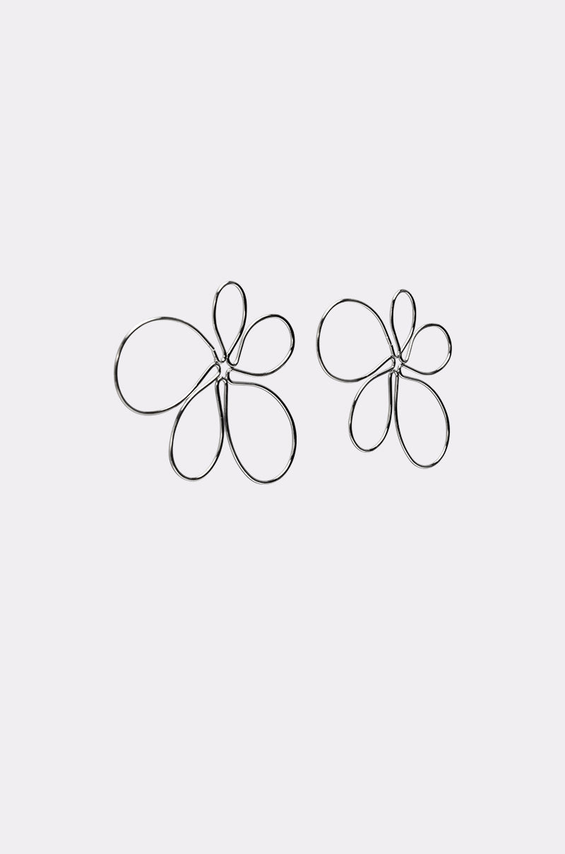 The LOVEY EARRING features two wire statement flower designs with silver-tone petals and abstract overlapping loops—one oversized, one smaller—displayed on a plain light background. 3