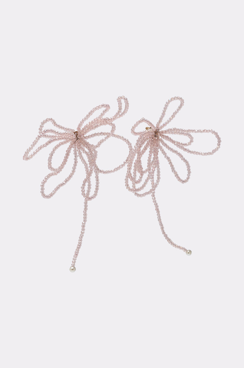 The GIRL PWR EARRING features two delicate, light pink beaded statement earrings in loose, oversized bow shapes with long, trailing ends, displayed against a plain light background. 4
