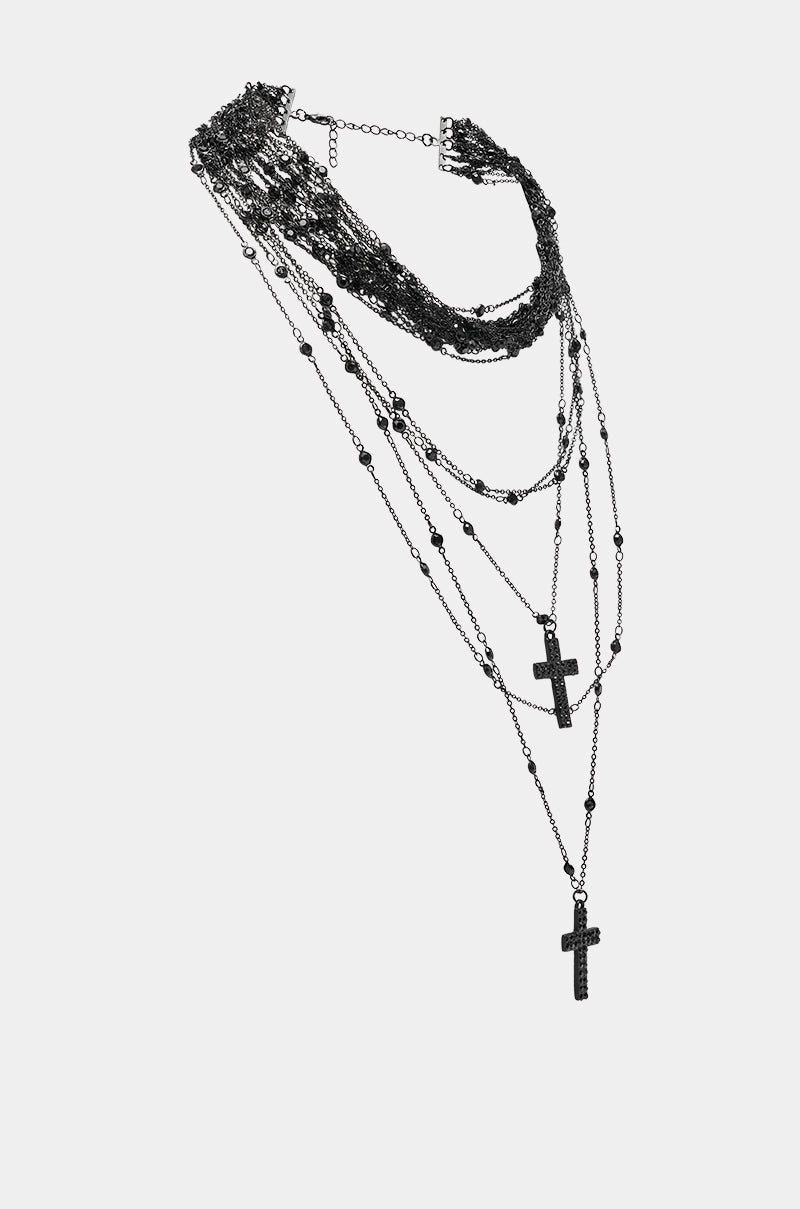 The DOLCE LAYERED NECKLACE features multiple thin black chains with beaded details and three cross pendants of varying lengths, perfect for a goth-inspired layered look, shown against a plain white background. 2