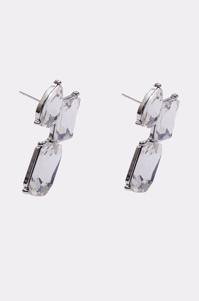 A pair of COUNTDOWN EARRING in silver-tone, showcasing three clear faceted geometric stones stacked vertically like clustered gemstones, displayed on a plain white background. 3
