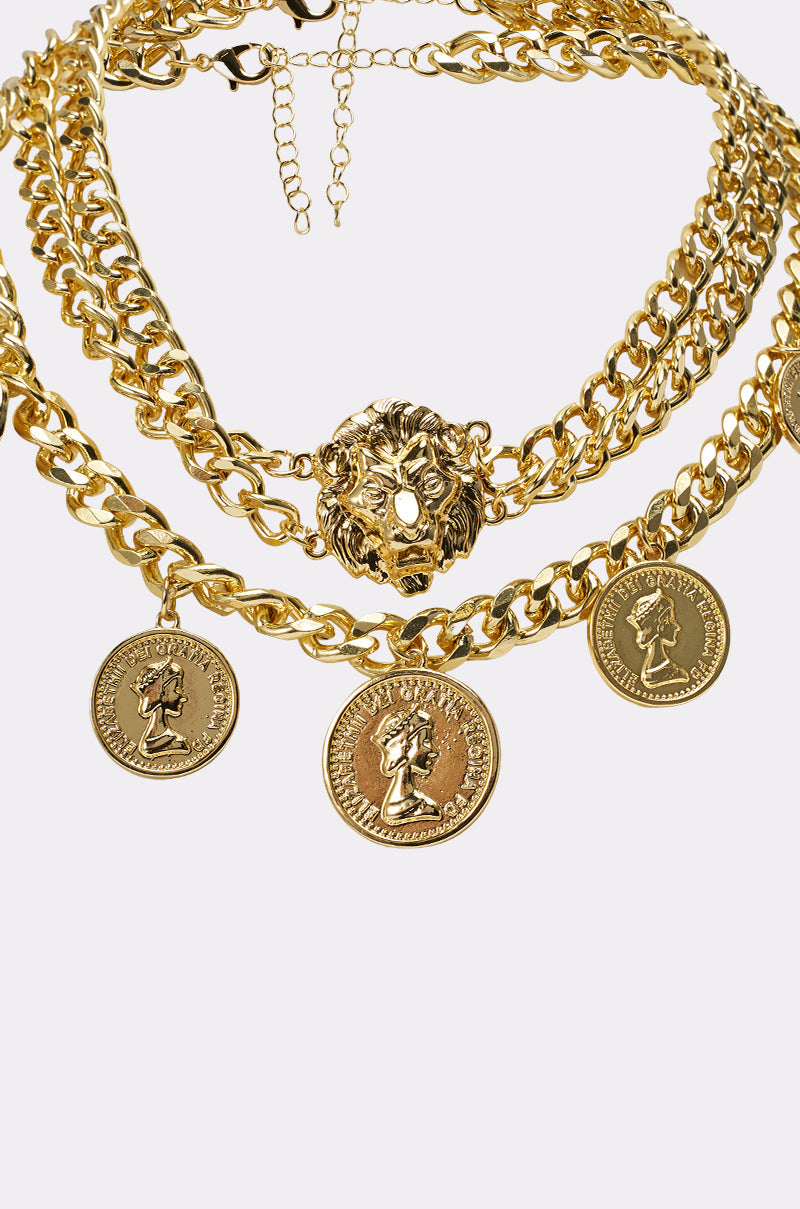 The AM WHO I THINK I AM NECKLACE is a chunky layered piece with a lion charm pendant and coin-shaped charms featuring classical profile designs, shown against a plain white background. 3