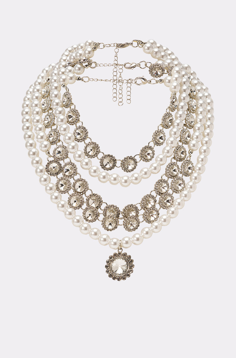 The AFFORD IT NECKLACE is a vintage-inspired statement piece with white pearl strands, ornate silver floral metalwork, and a central pearl pendant framed in intricate silver, displayed on a white background. 0