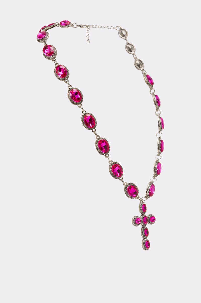 The NELLY NECKLACE is a crystal statement piece with large oval pink gemstones, smaller clear stones, and a bold cross pendant of matching pink gems, shown on a simple light background. 3