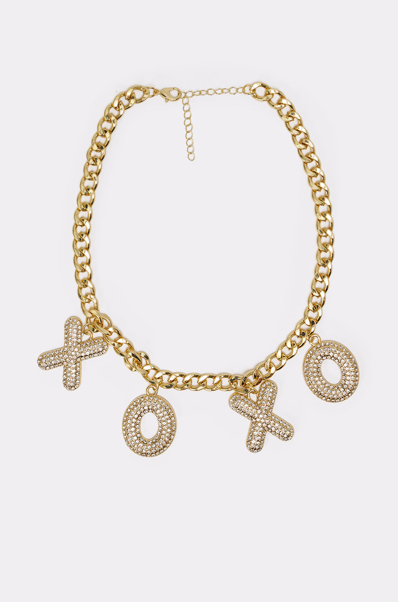 The KISSES NECKLACE is a chunky chain necklace with three gold-tone XO letter charms pavé-set with clear rhinestones, shown on a plain white background. 5