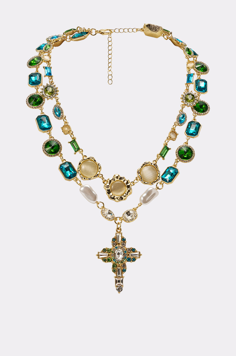 The ON A YACHT NECKLACE features layered vintage-inspired chains with green, blue, and clear gemstones and a jeweled cross pendant—an elegant statement piece for evening wear. 0