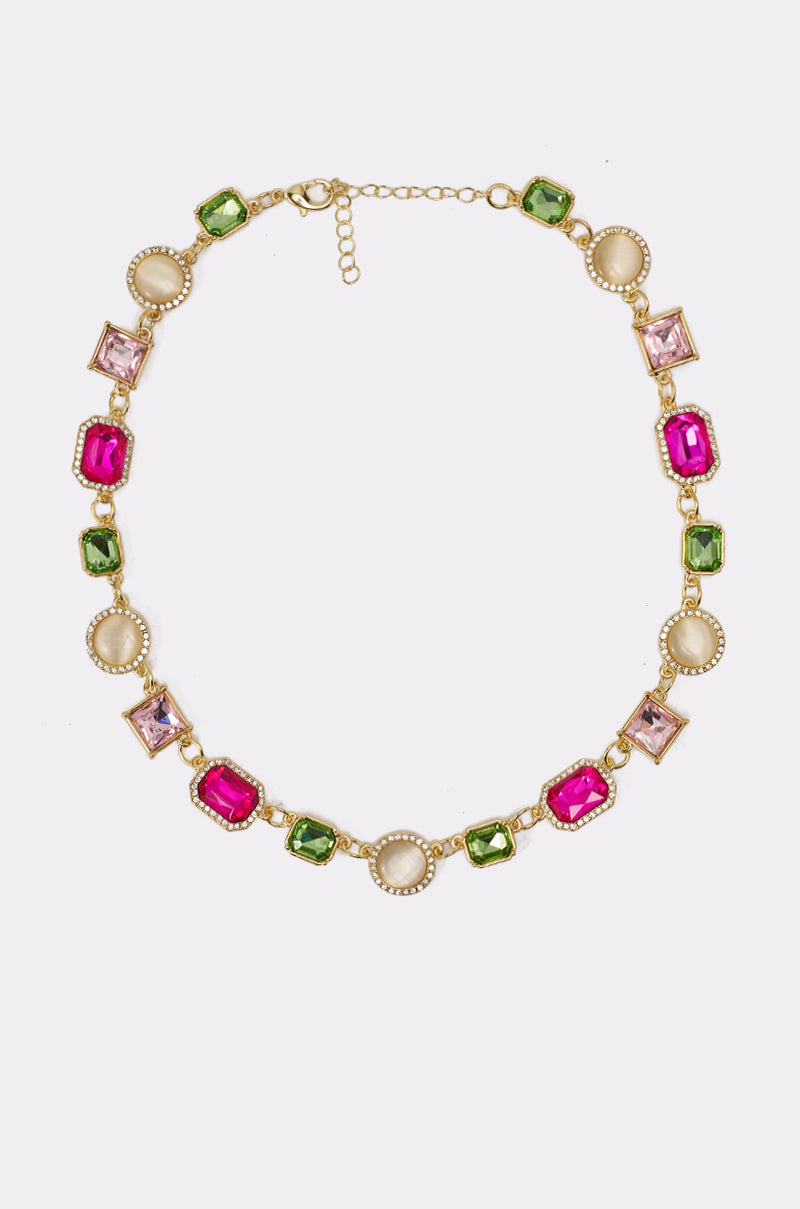 The WHO DO IT LIKE ME NECKLACE features alternating square and round pink, green, light purple, and creamy white gemstones in gold bezel settings, displayed against a white background. 0