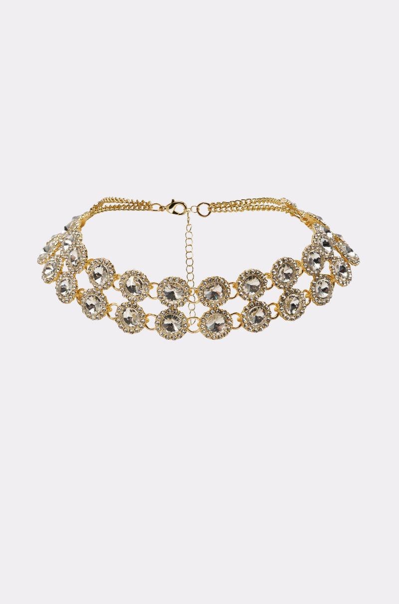The RIRI NECKLACE is a gold-tone collar with two rows of large circular clear gemstones, each bordered by smaller crystals, creating a stunning adjustable statement choker. 0