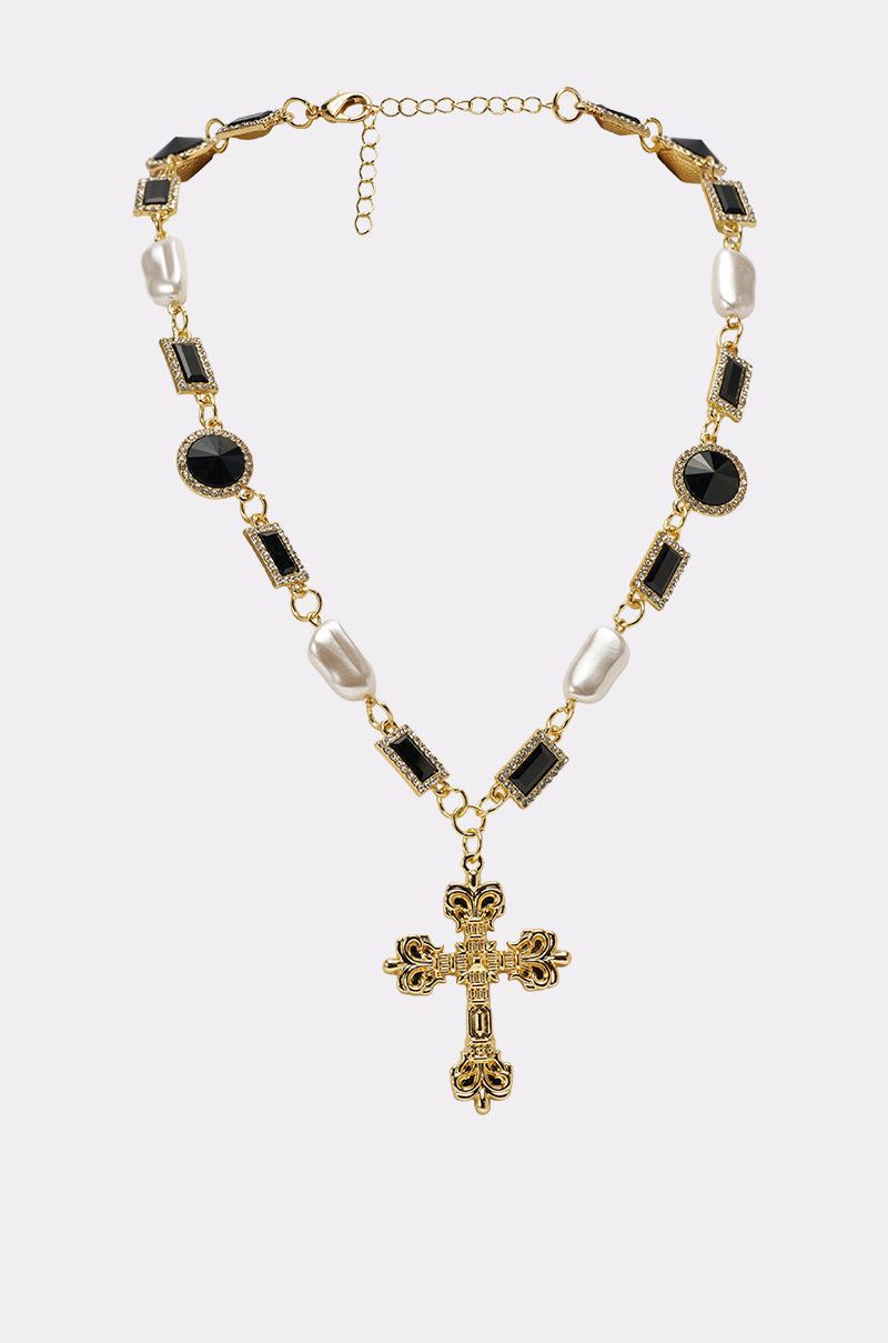 The WITH THE TIMES NECKLACE is a gold-tone chain cross necklace with a decorative pendant, featuring black gemstones and white pearls alternating along the chain, shown on a plain light background for gothic-glam elegance. 1